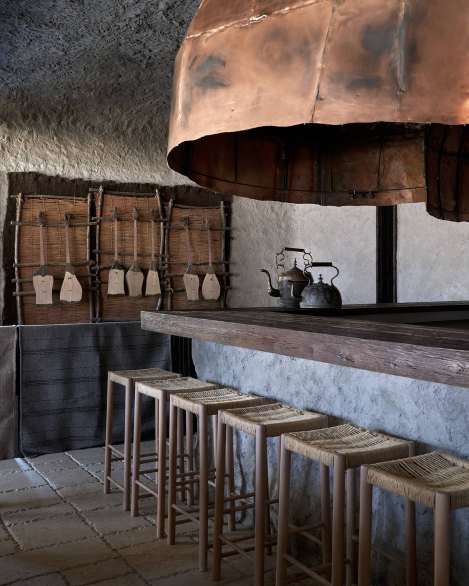 Industrial kitchen featuring wooden stools, a rustic copper hood, and concrete walls