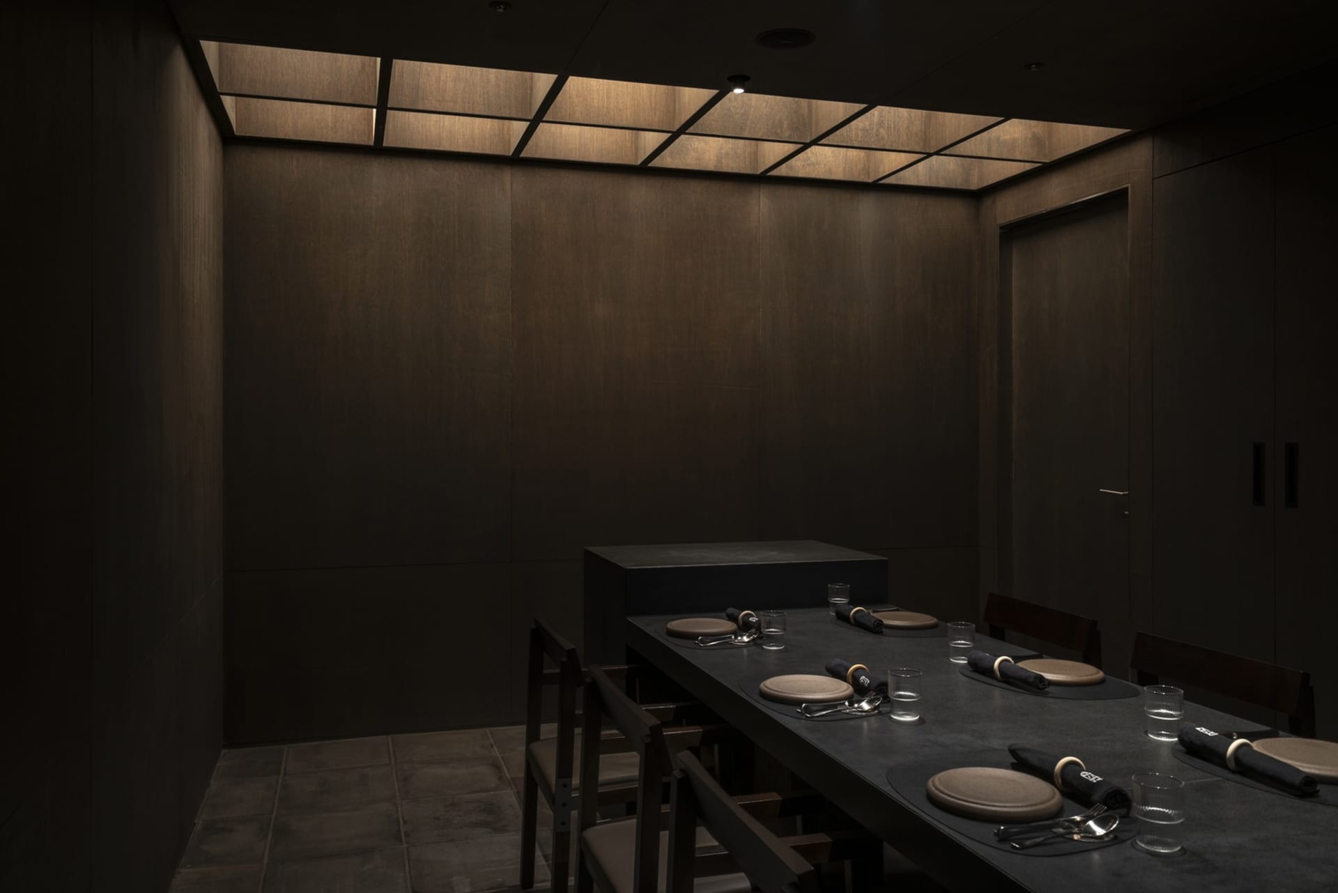 昏暗光線的工業風餐廳室內,長形深色餐桌已擺設餐具,並搭配金屬元素。