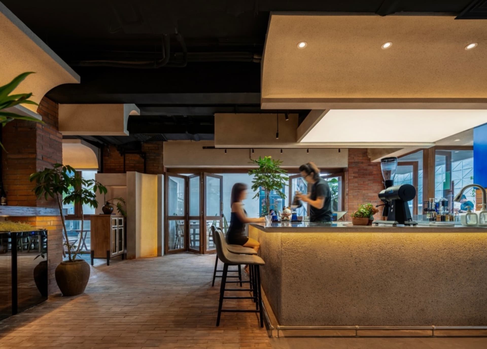 A modern coffee shop features a sleek concrete bar counter and seating area with a person sitting on a stool.