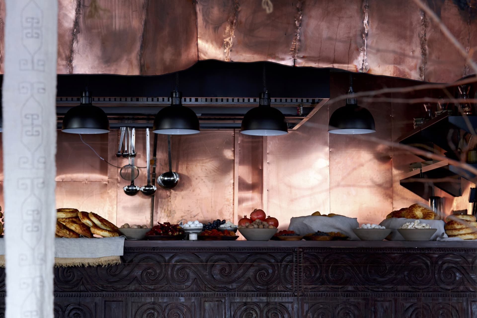 A commercial kitchen with copper walls and a dark, intricately carved wooden counter.