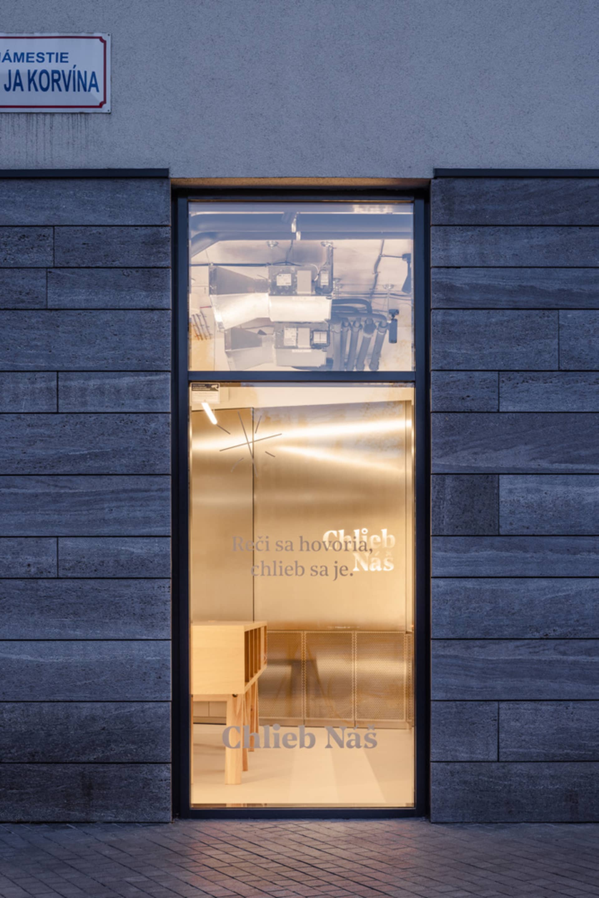 A glass storefront with a sign reading 'Chlieb Nas' and reflective surface.