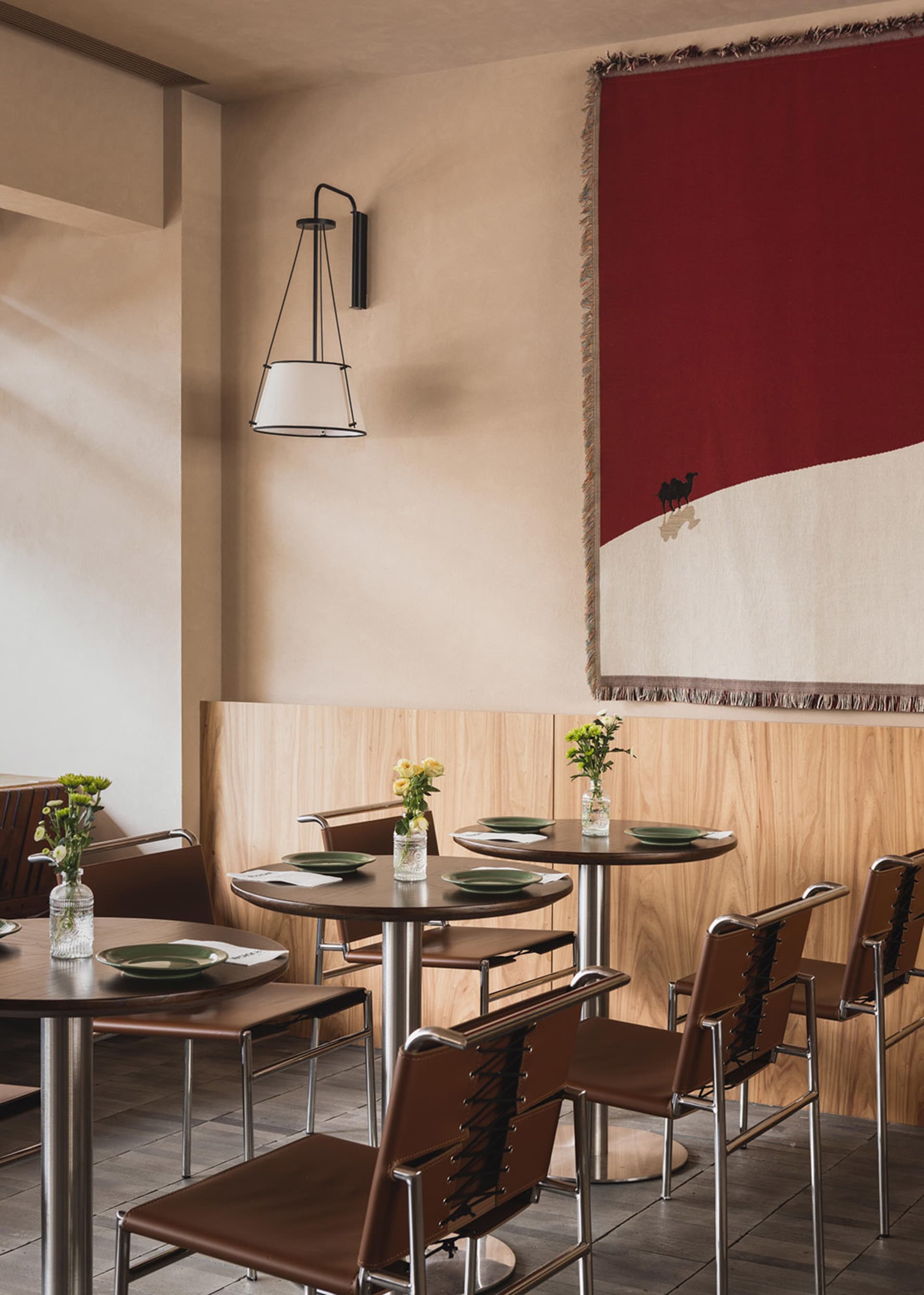 A modern cafe interior featuring a red wall tapestry with a camel design.
