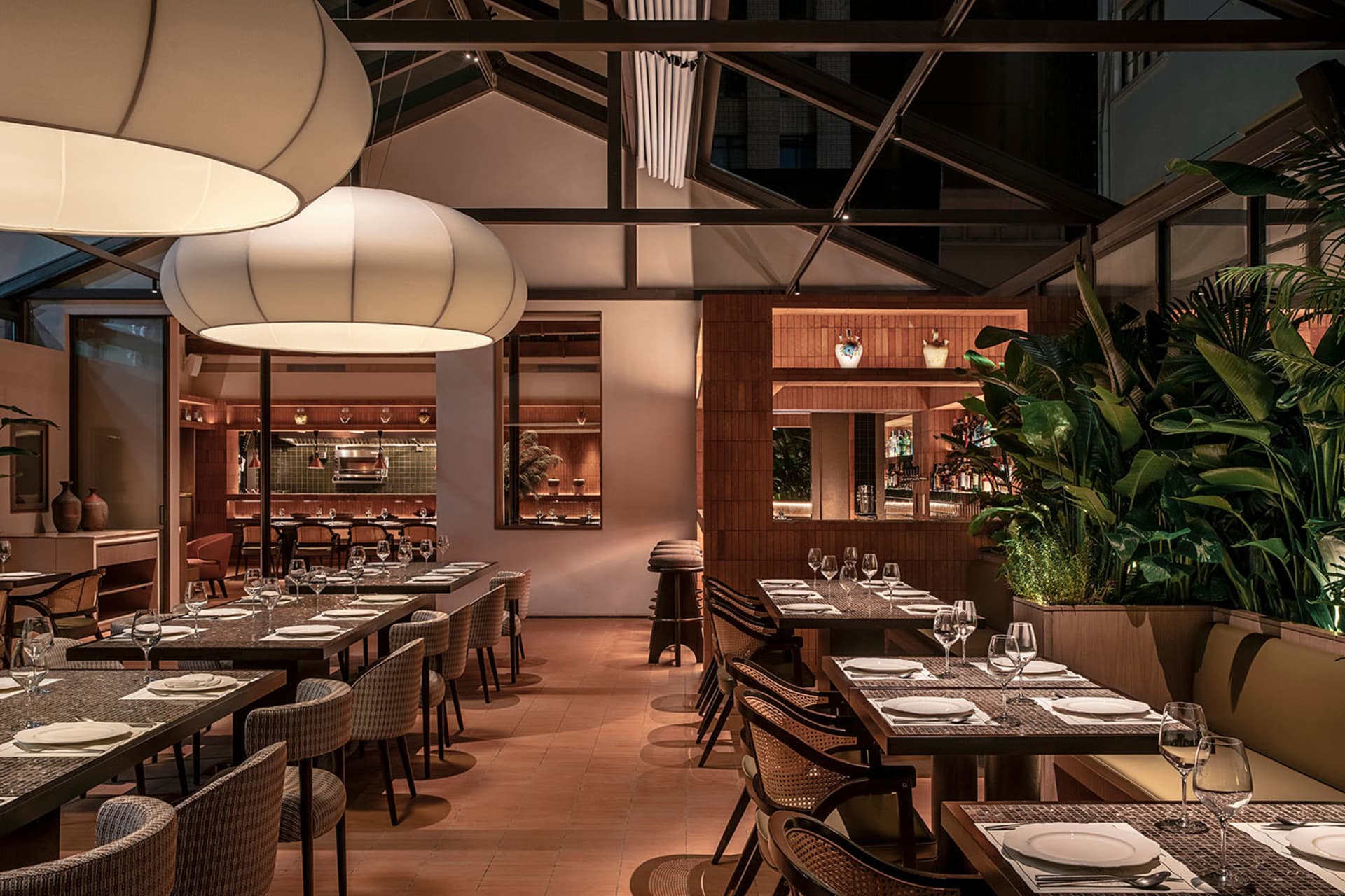 Modern restaurant interior with industrial design elements, featuring wood furniture, glass lighting, and greenery.