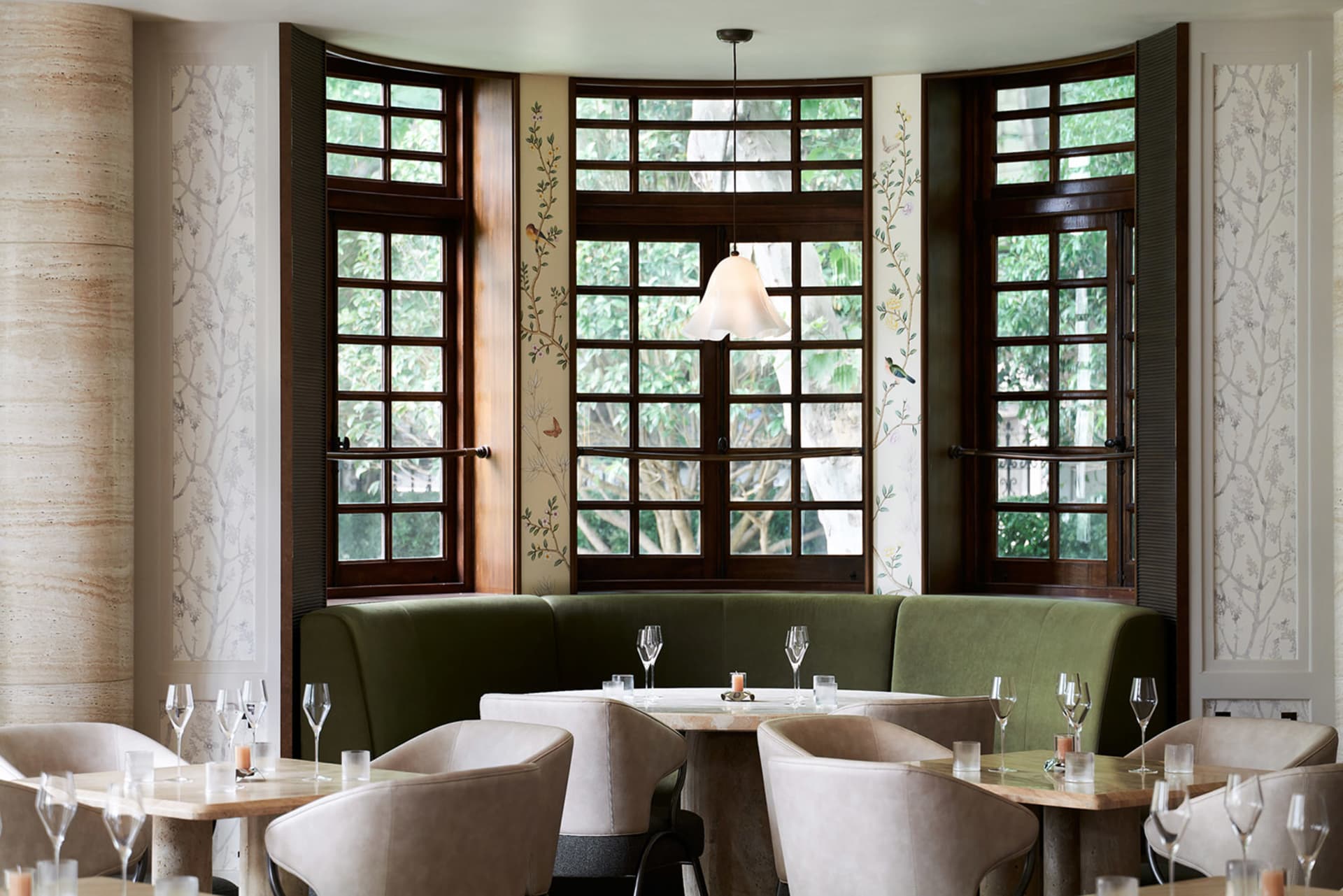 An elegant restaurant interior with green sofas, glass tables, and wooden accents