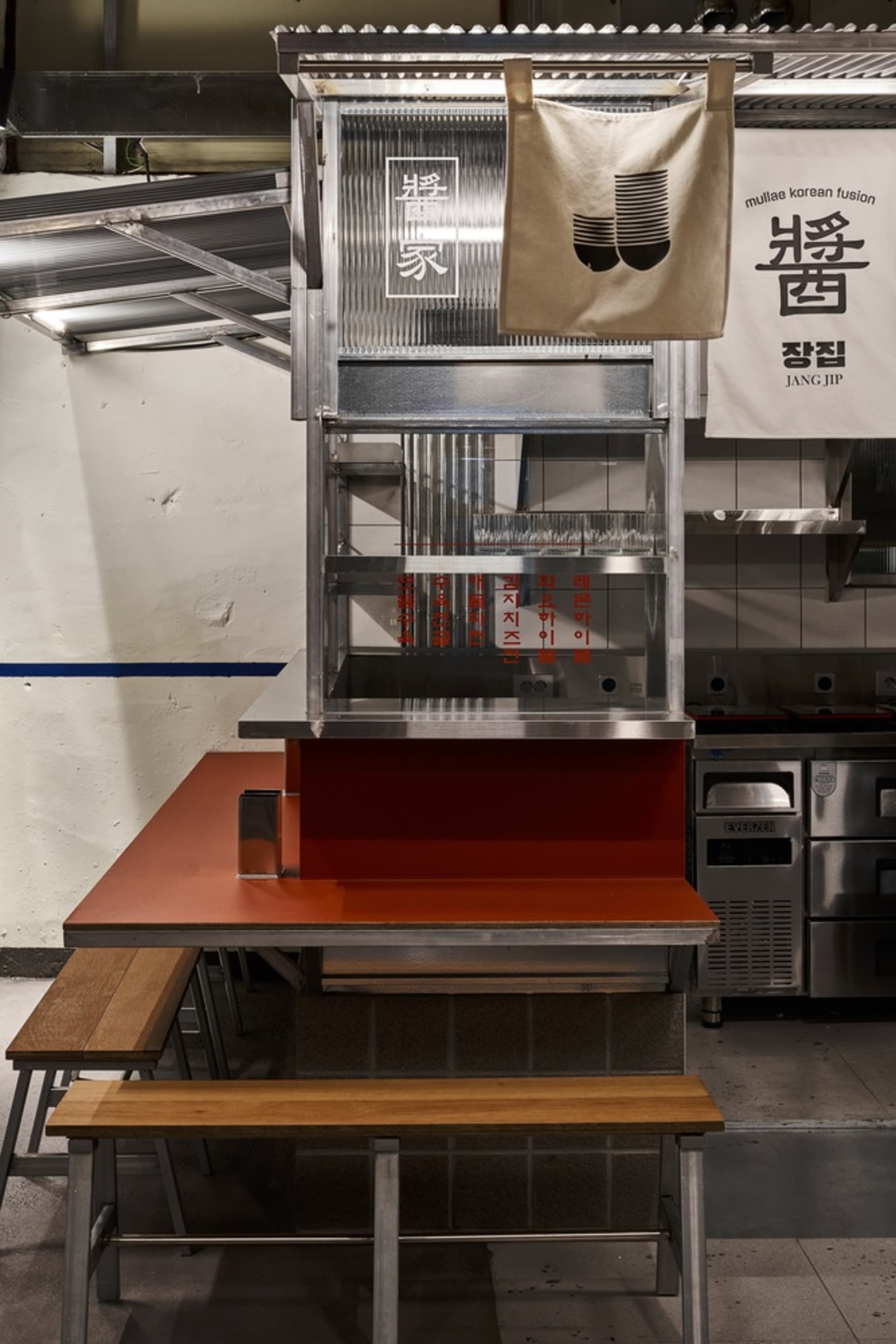 極簡餐廳室內,設有金屬餐檯、木製長椅及韓文招牌。
