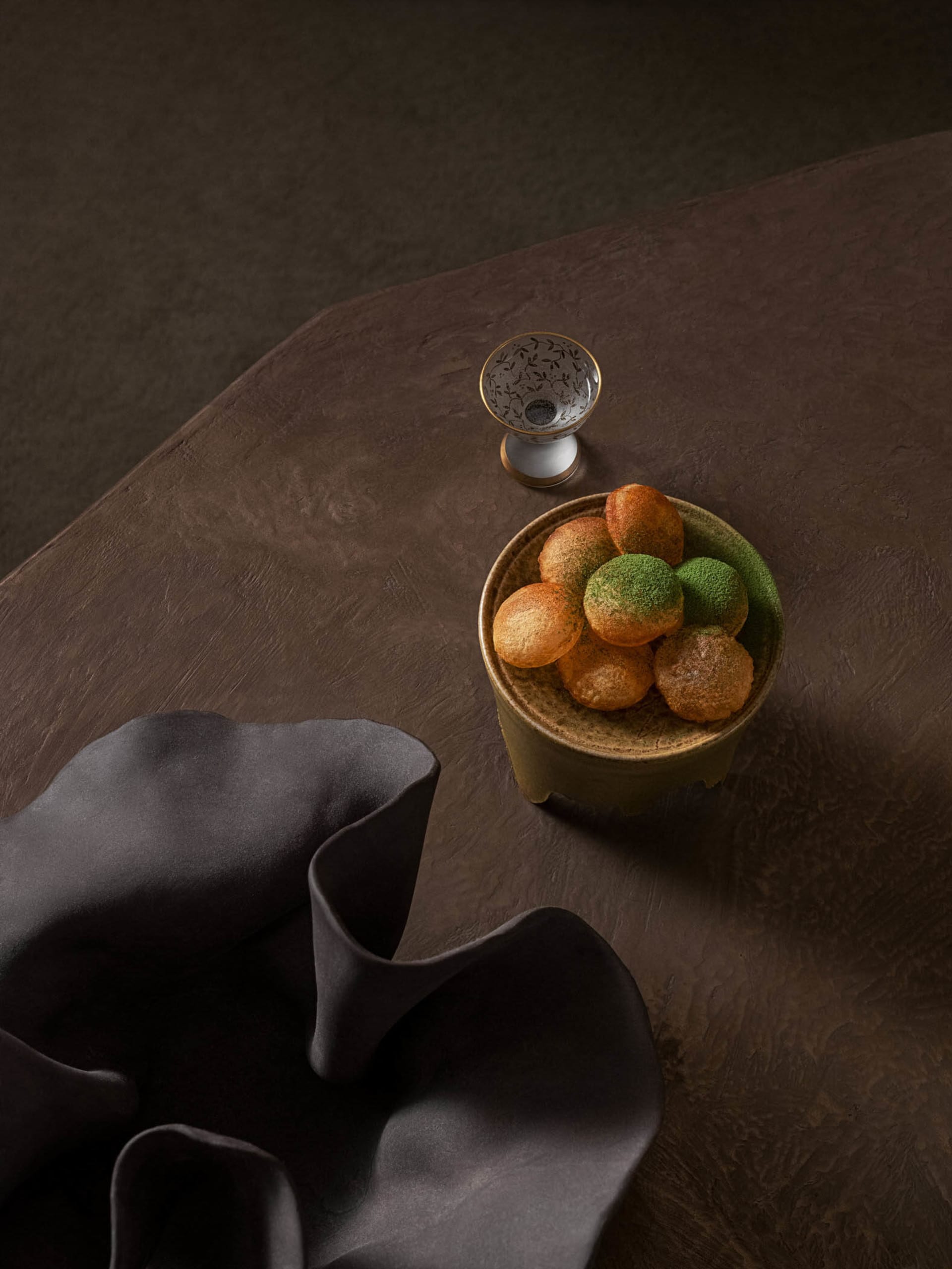 A ceramic bowl filled with round, golden-brown objects covered in a green powder, placed on a textured brown table next to a