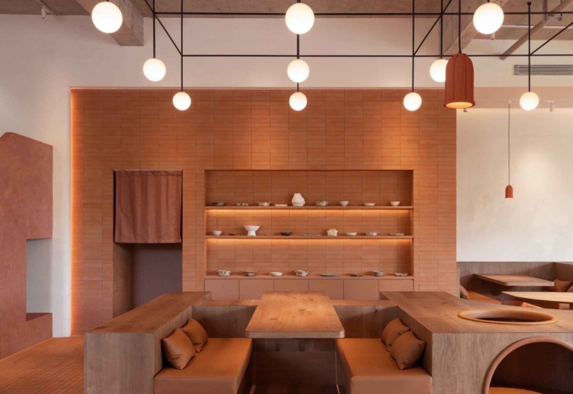 A modern restaurant interior with terracotta walls and wooden seating and fixtures.