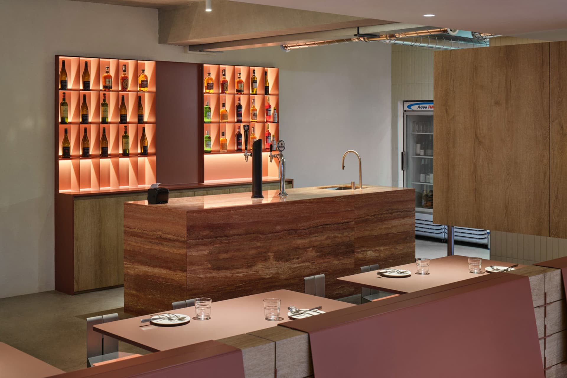 A modern bar with a marble counter featuring illuminated shelves filled with various bottles.
