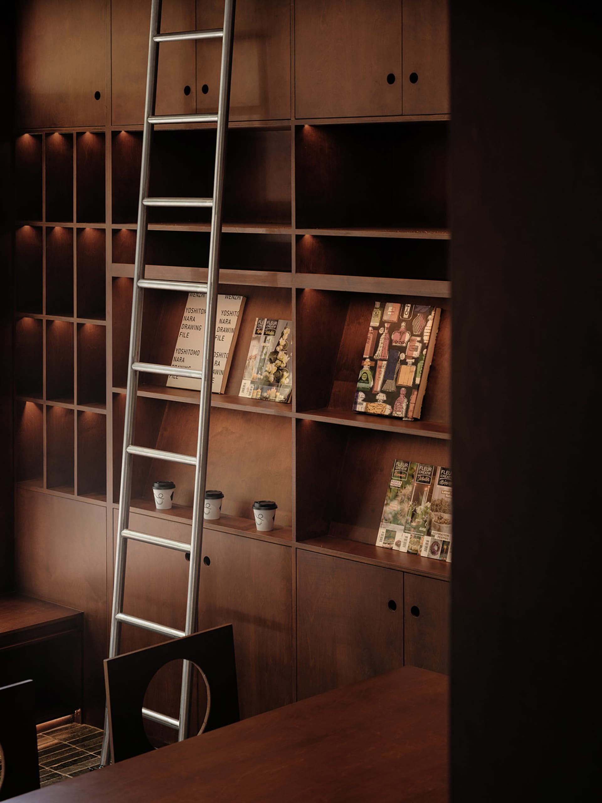 A modern library with wooden bookshelves and a ladder for accessing the higher shelves.