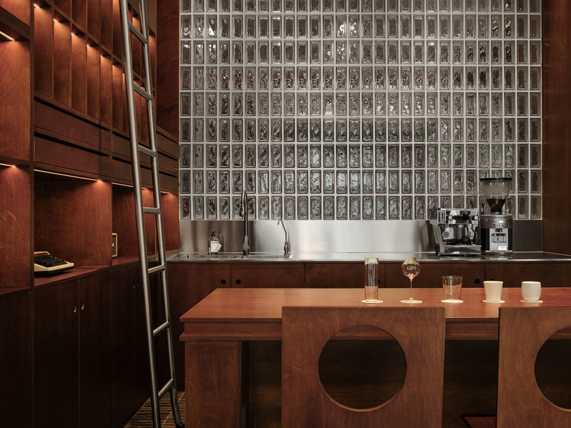 Modern minimalist commercial kitchen with glass cabinets, wood furniture, and a large glass block wall.