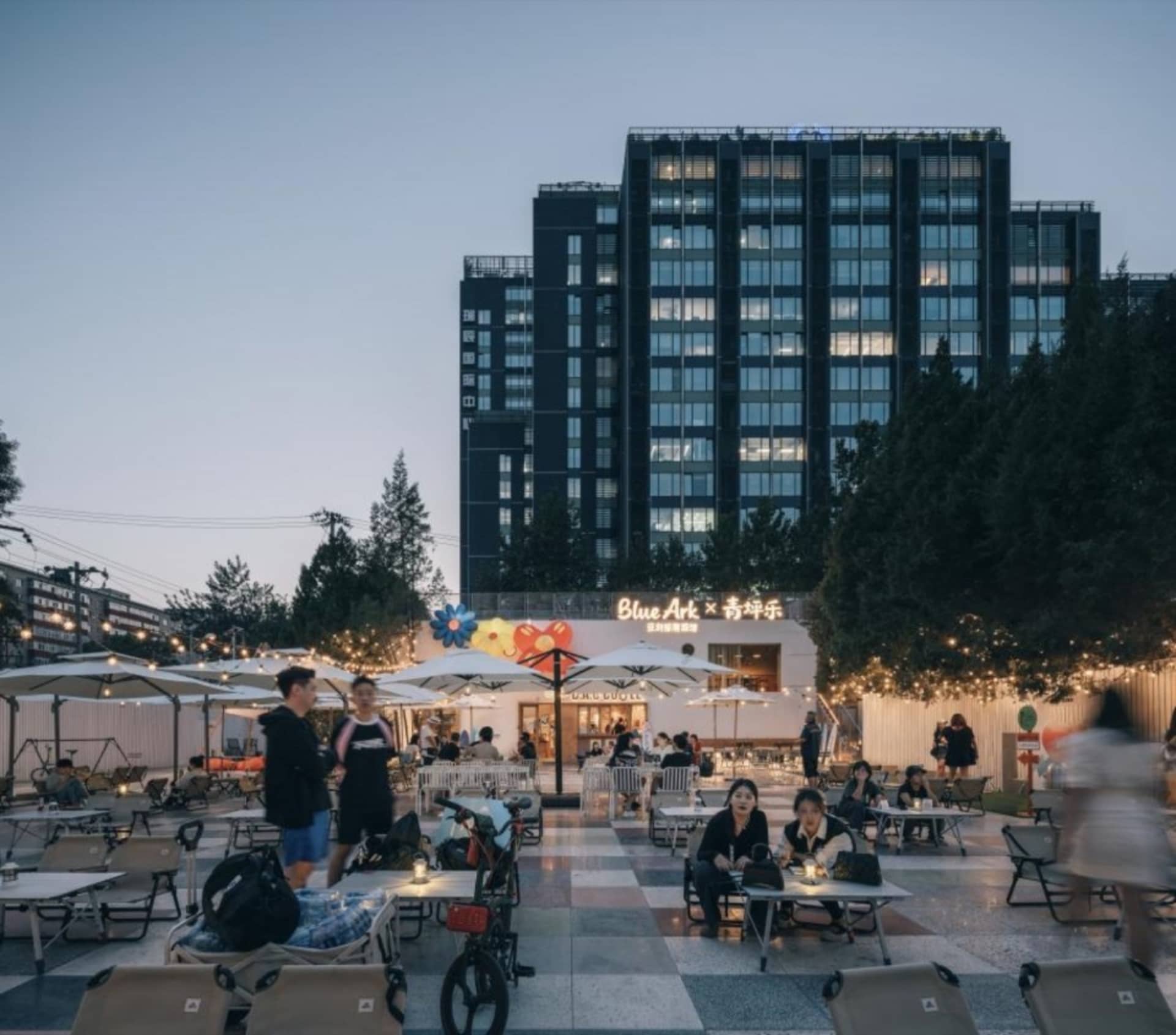 An outdoor cafe with concrete flooring, lighting umbrellas, and a high-rise building in the background.