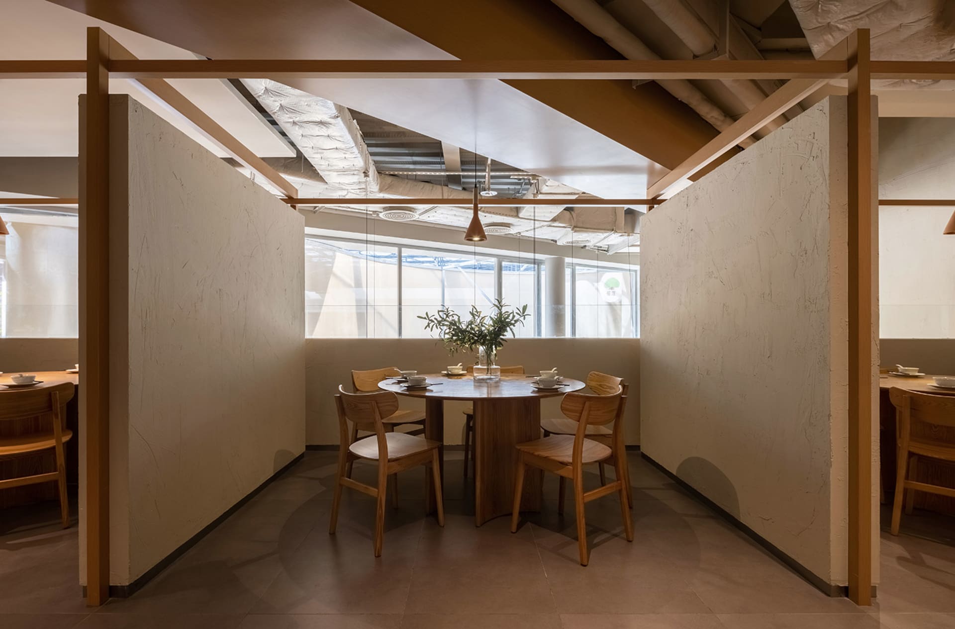 A modern restaurant interior designed with wooden tables and concrete flooring, featuring a round table, chairs, and minimali