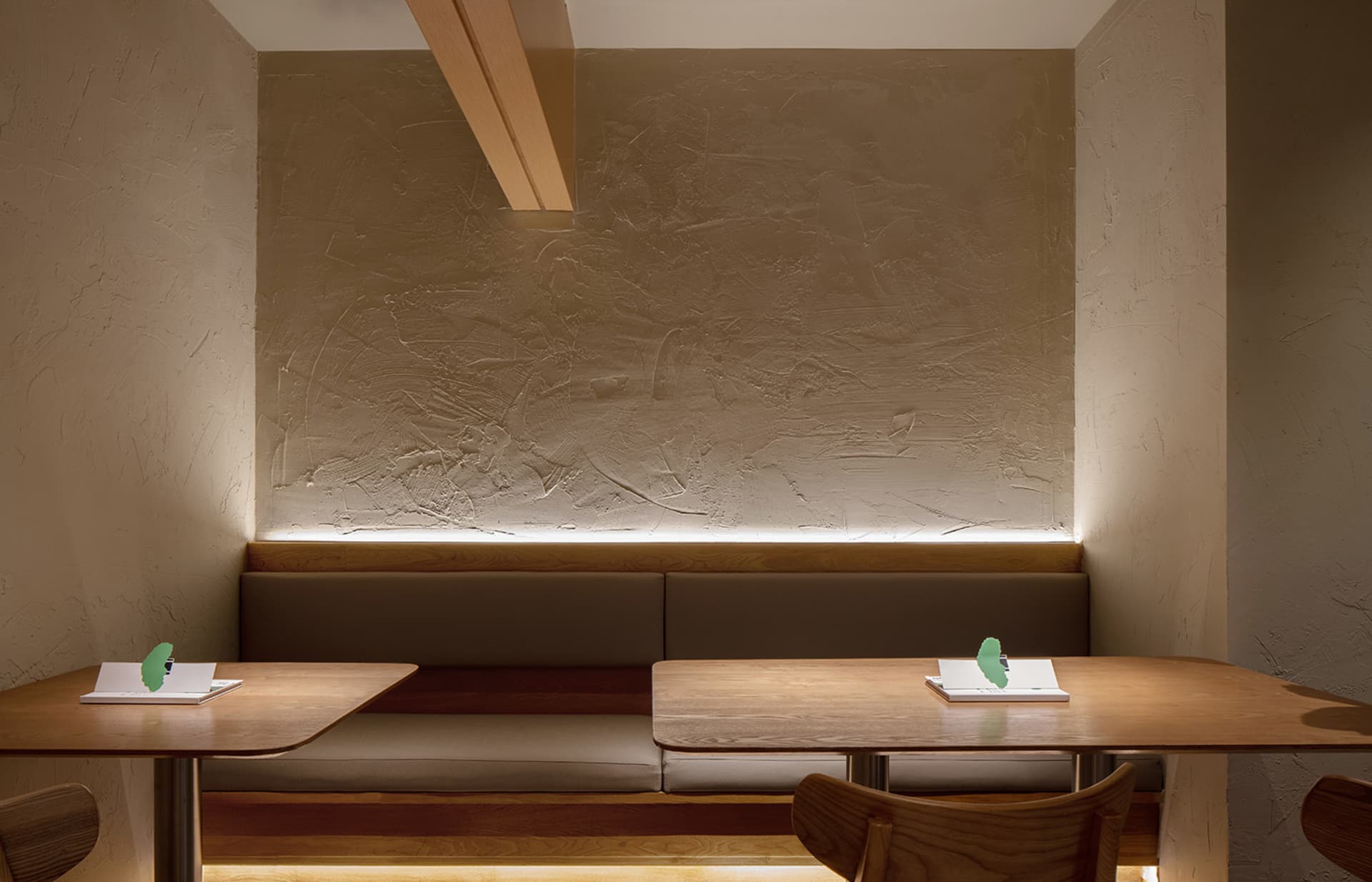A modern restaurant interior with wooden tables and benches, featuring a textured wall and ambient lighting