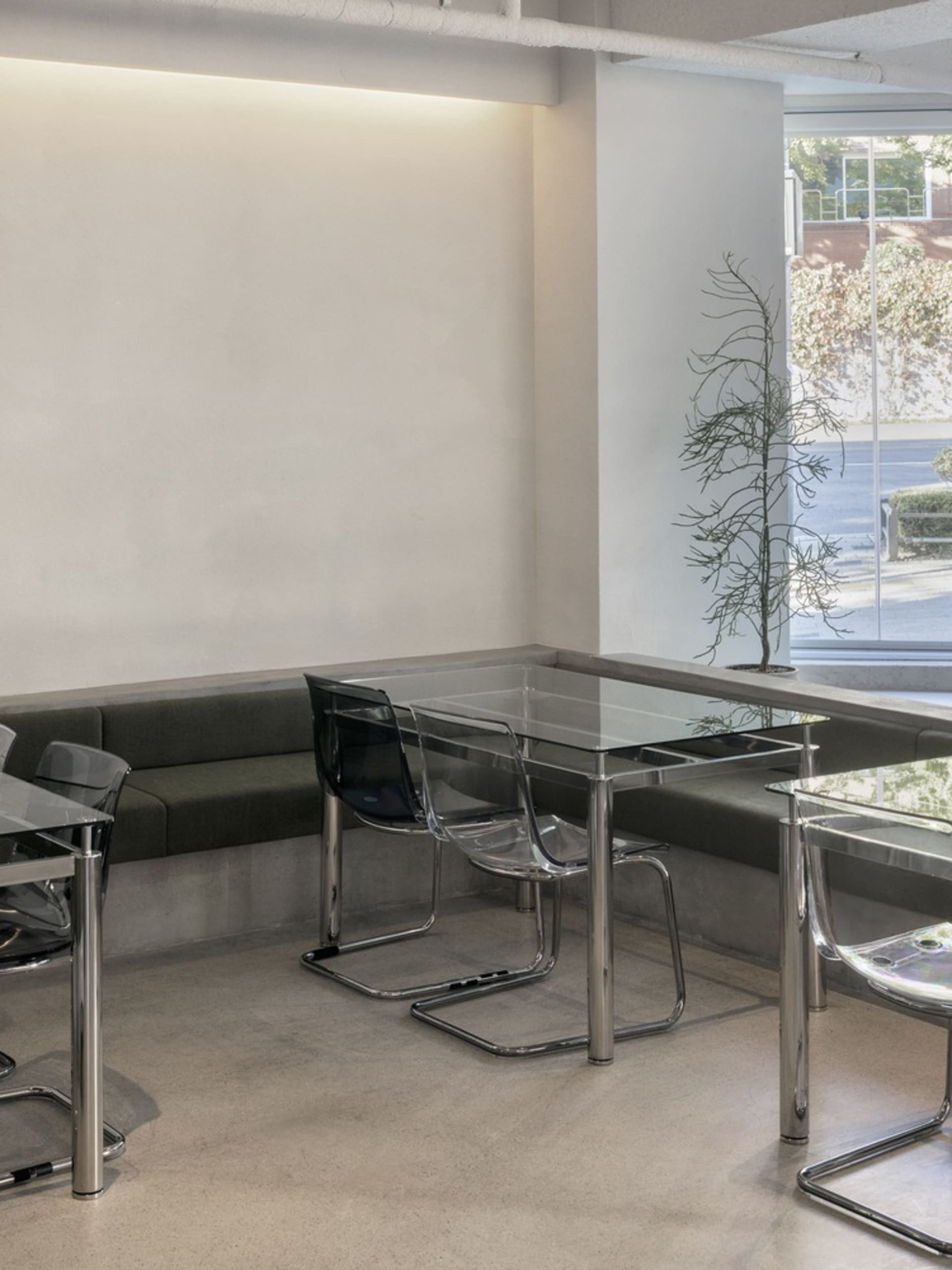 A modern industrial restaurant interior featuring glass tables, concrete bench seating, and a canvas wall.