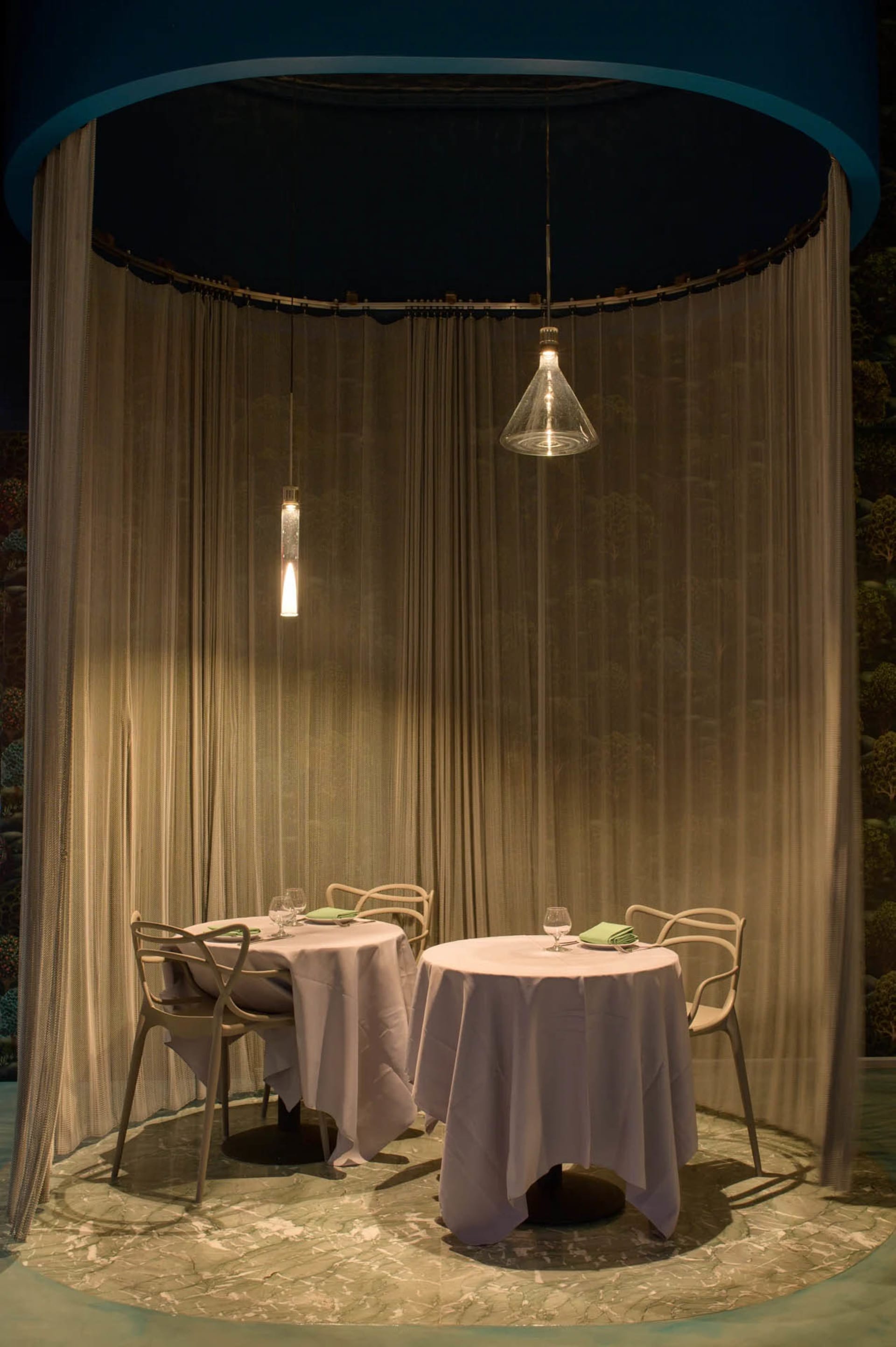 A restaurant capsule with white marble floors, white tables, and white chairs surrounded by white translucent fabric curtains