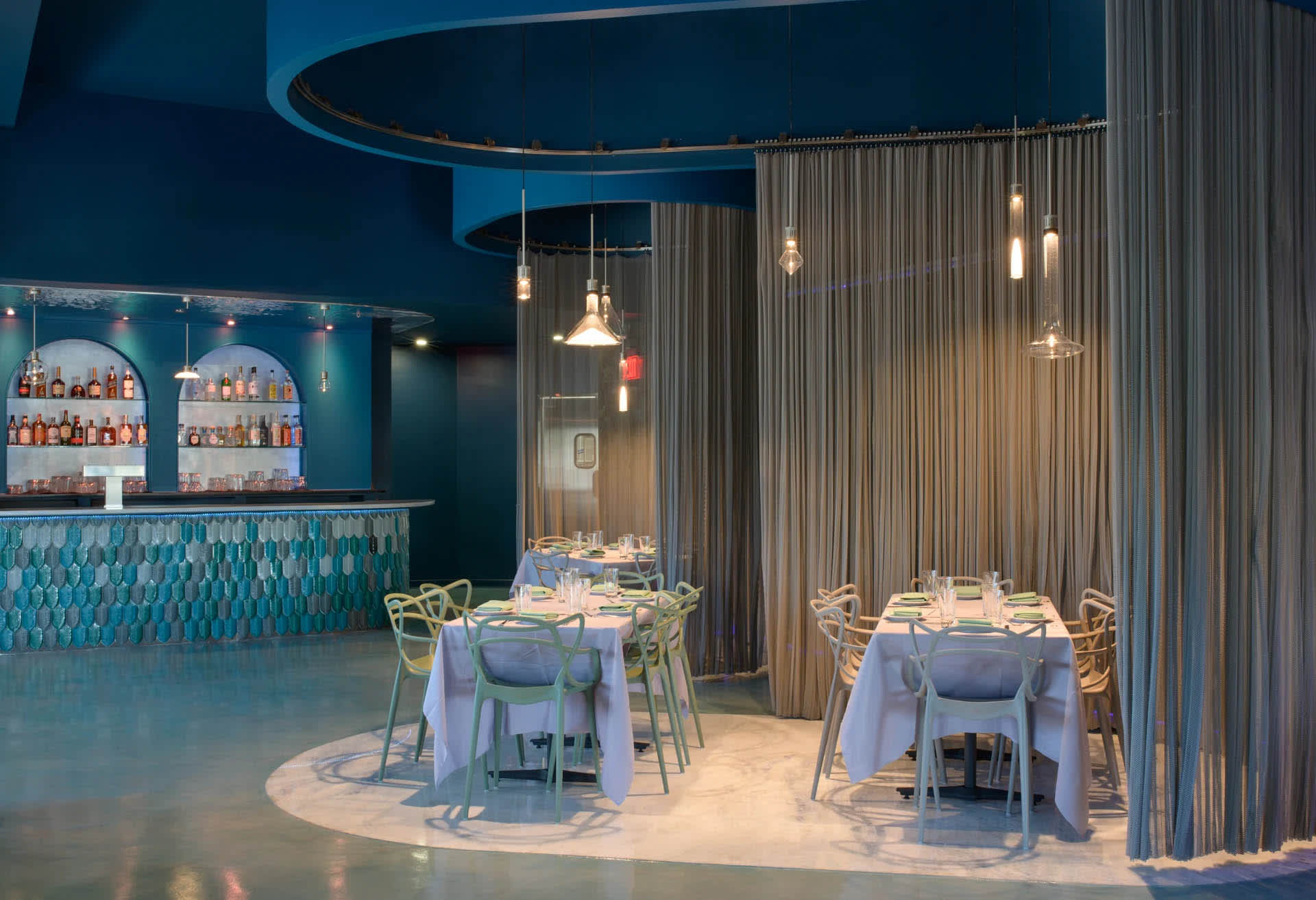 A modern, industrial interior design of a restaurant featuring metallic finishes, glass elements, and translucent curtains.