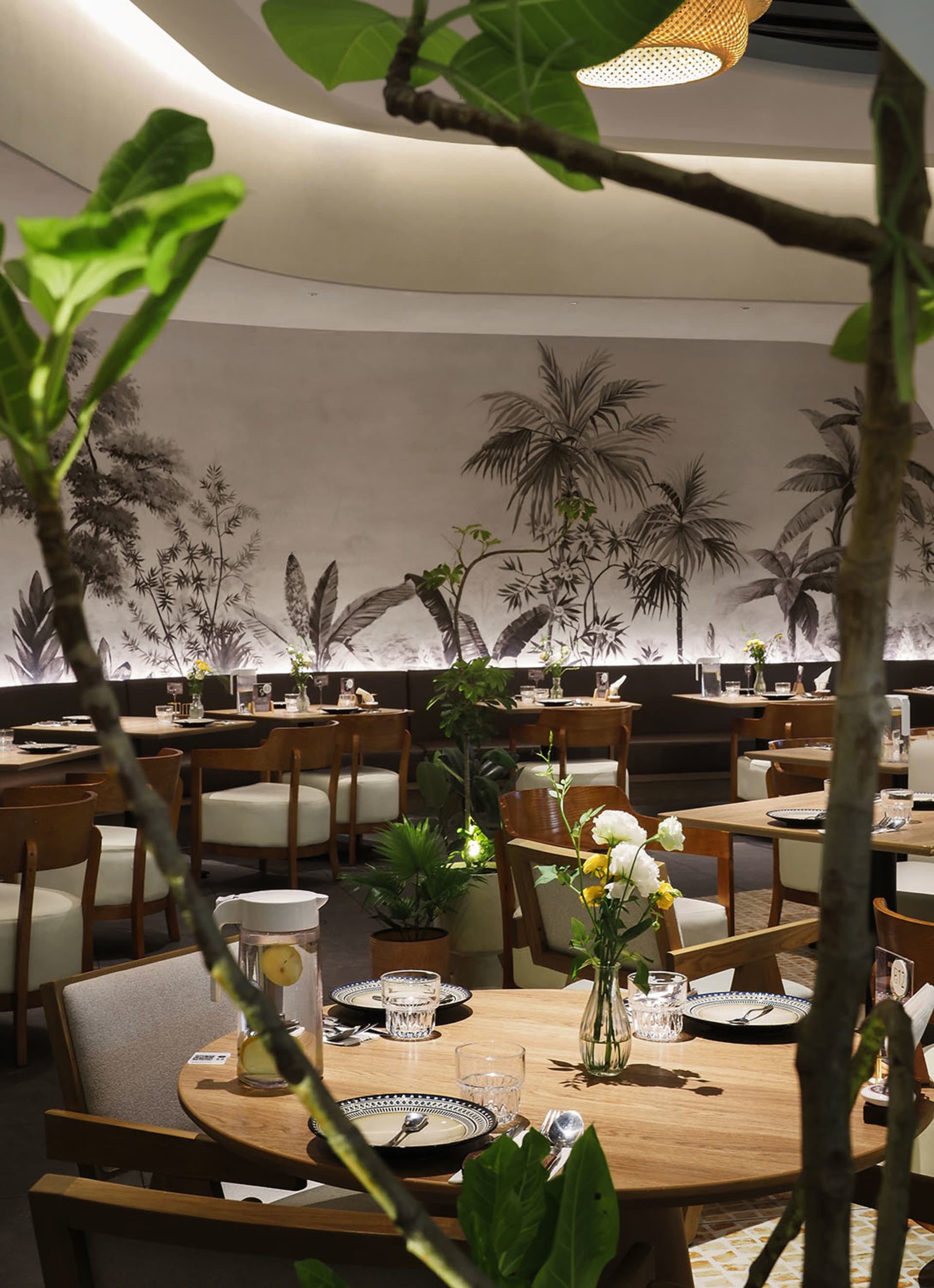 Lushly decorated cafe with wooden furniture and plant life on tables and walls.