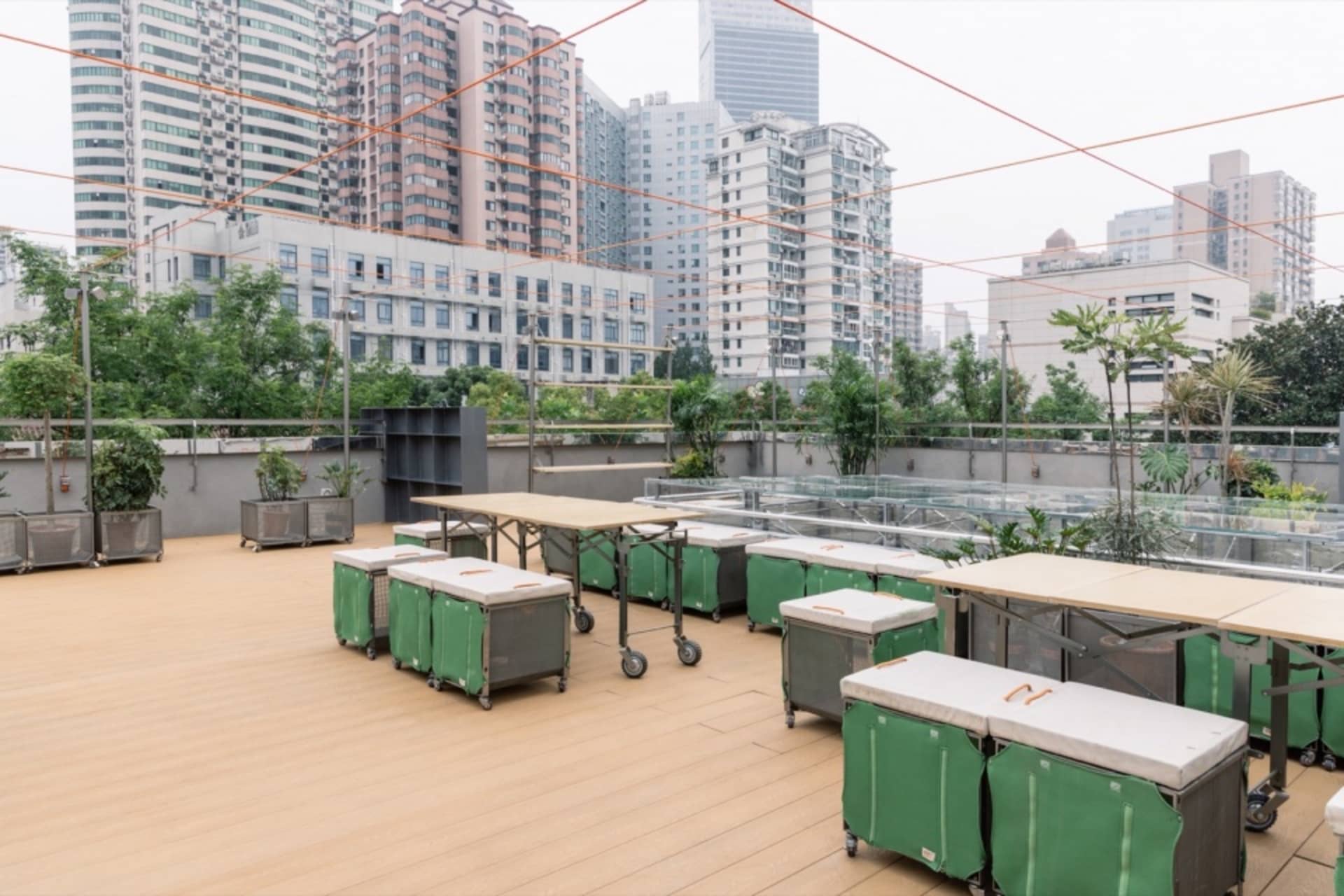 屋頂咖啡廳設有桌椅與綠色帆布容器，背景為城市景觀。