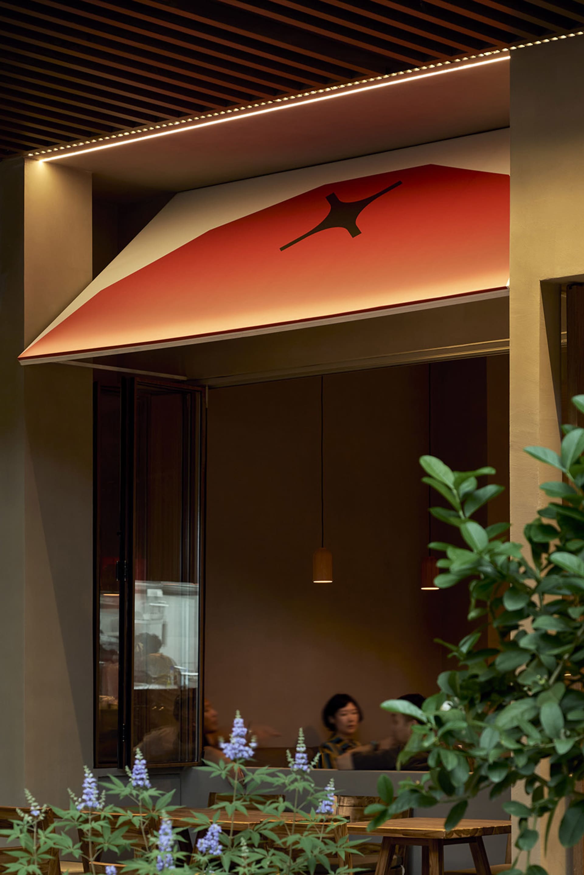 Outdoor seating area with wooden tables and chairs in front of a restaurant with a wooden ceiling and red awning