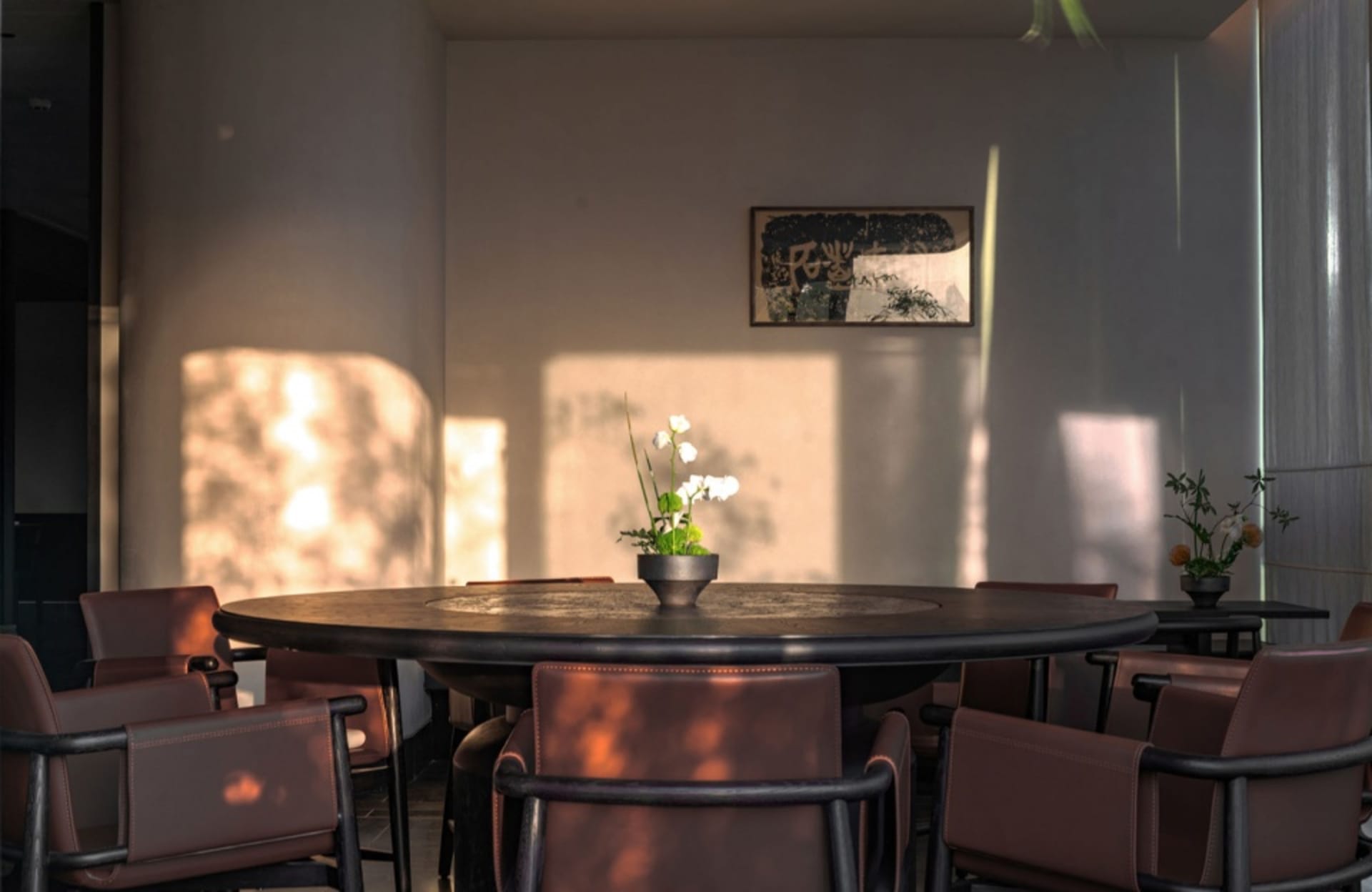 A well-lit, modern restaurant interior with a round dining table, brown leather chairs, and a potted plant.