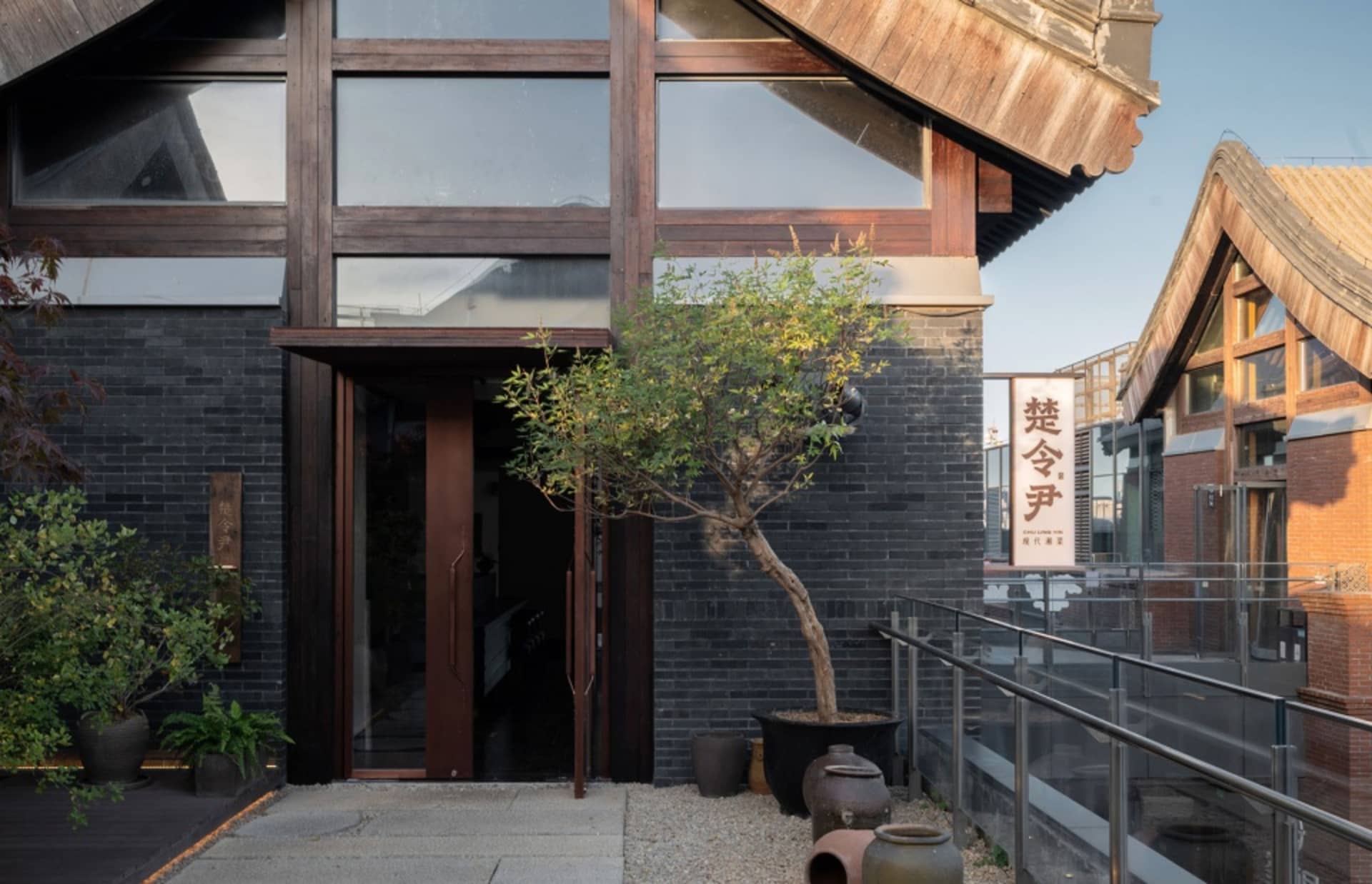 Modern restaurant exterior with brick and concrete materials, featuring black bricks and a potted tree.
