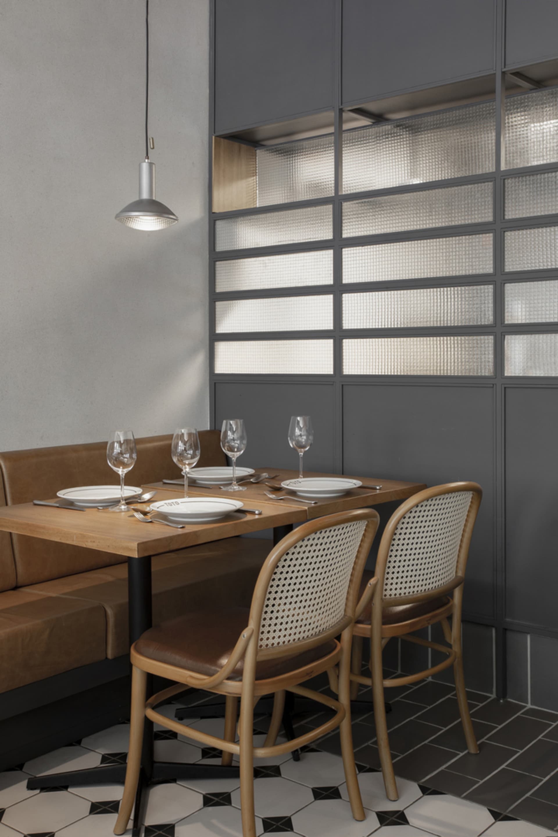 A modern restaurant setting with a table set for dinner, featuring wooden chairs, glass windows, and a leather booth seat.