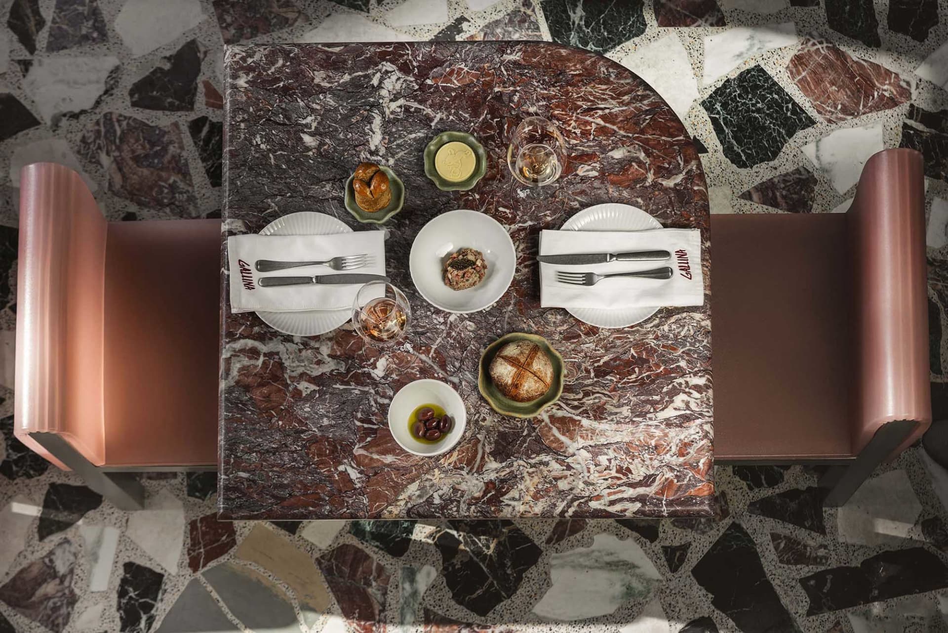 A restaurant table with a marble tabletop, set with plates, cutlery, and bread.