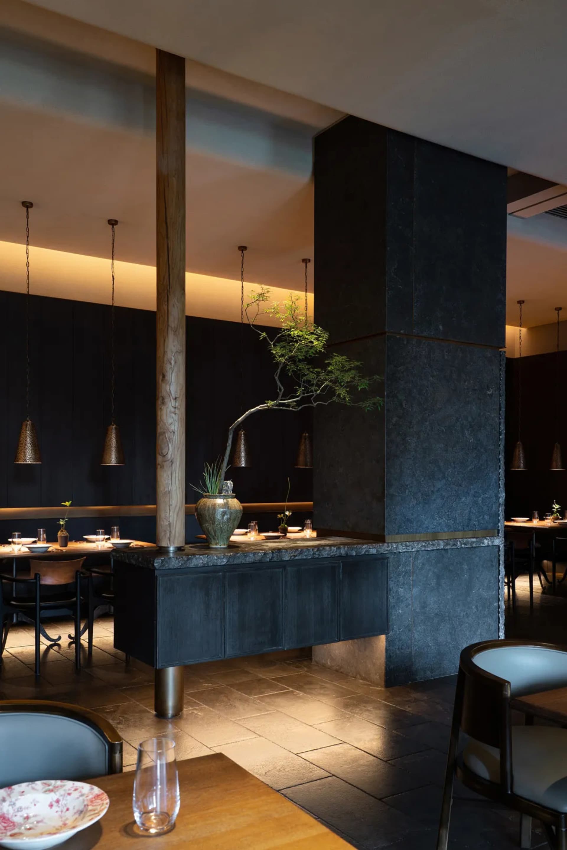 A modern, industrial restaurant interior featuring stone columns and metal framed windows.