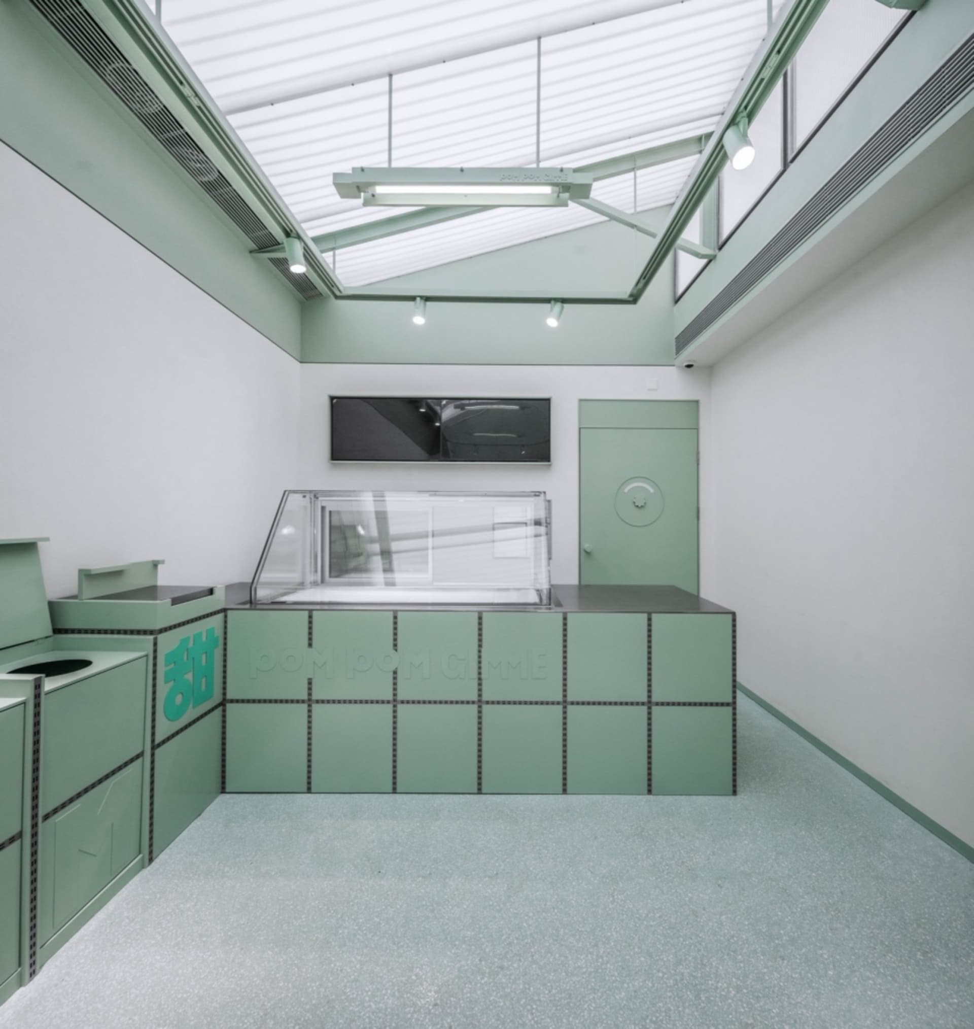A modern cafe interior with a green panel-covered counter, glass display case, and minimalist design.