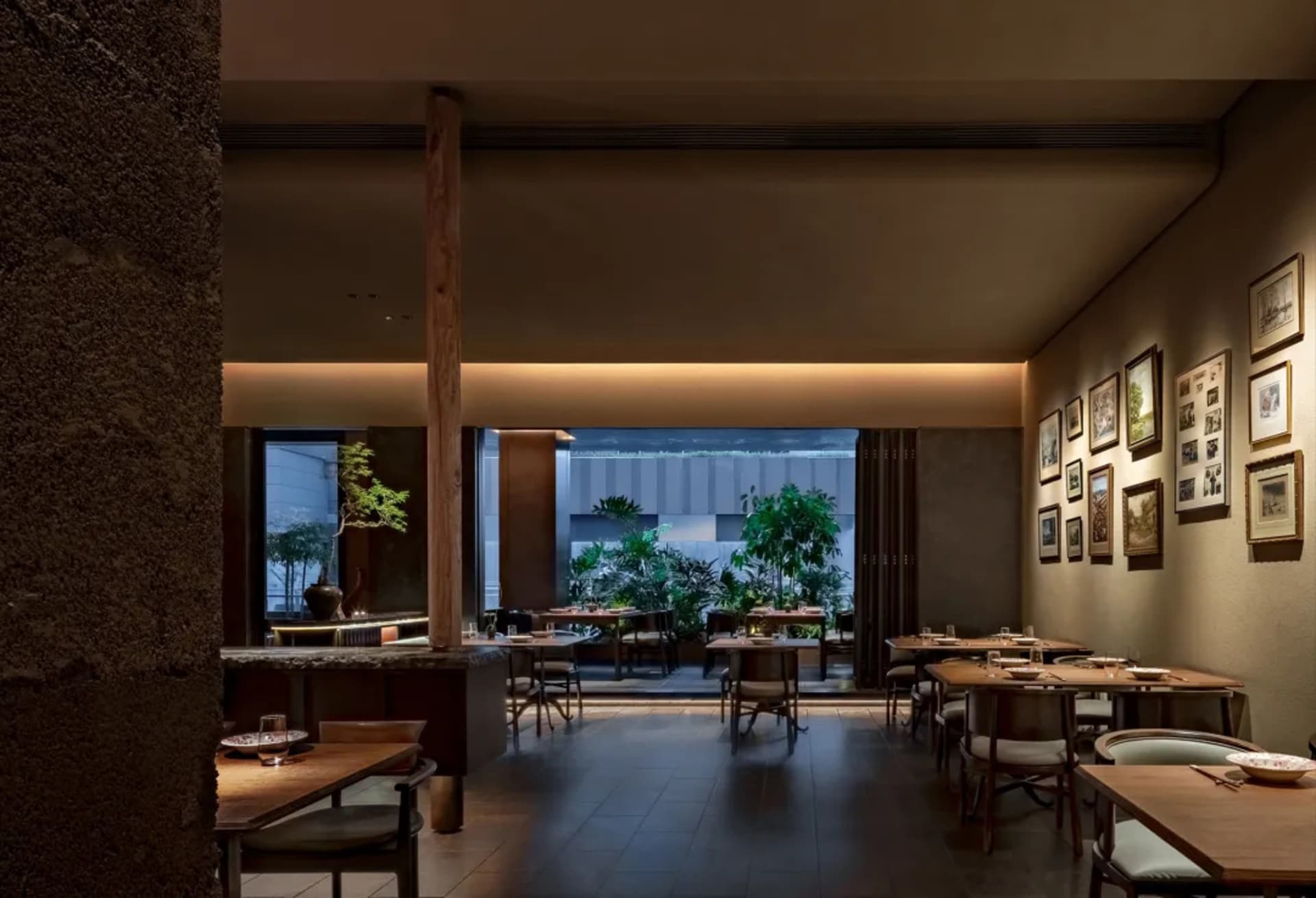 A modern restaurant interior featuring wooden tables, stone details, and green plants.