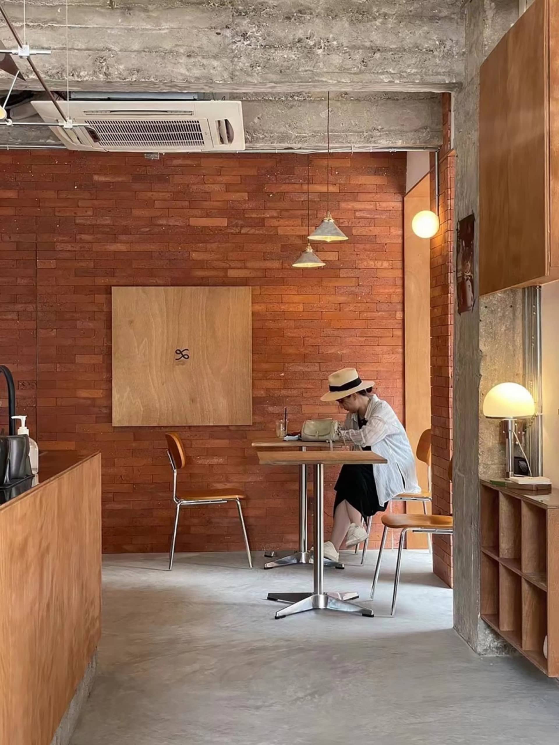 A person wearing a white shirt, black skirt, and beige hat sitting at a table in a coffee shop with brick walls and wooden fu