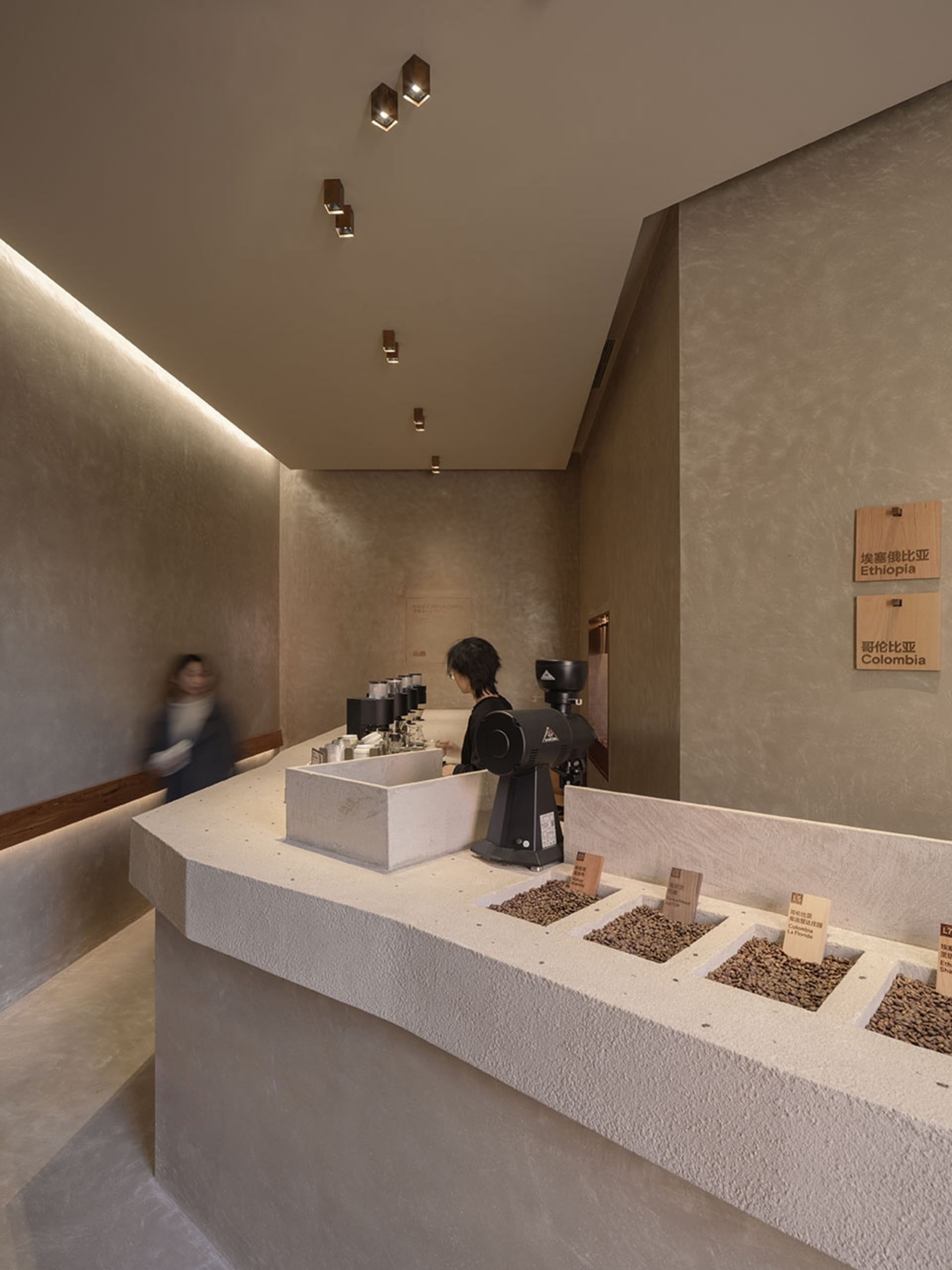 A modern coffee shop with a concrete counter displaying coffee beans from different origins.