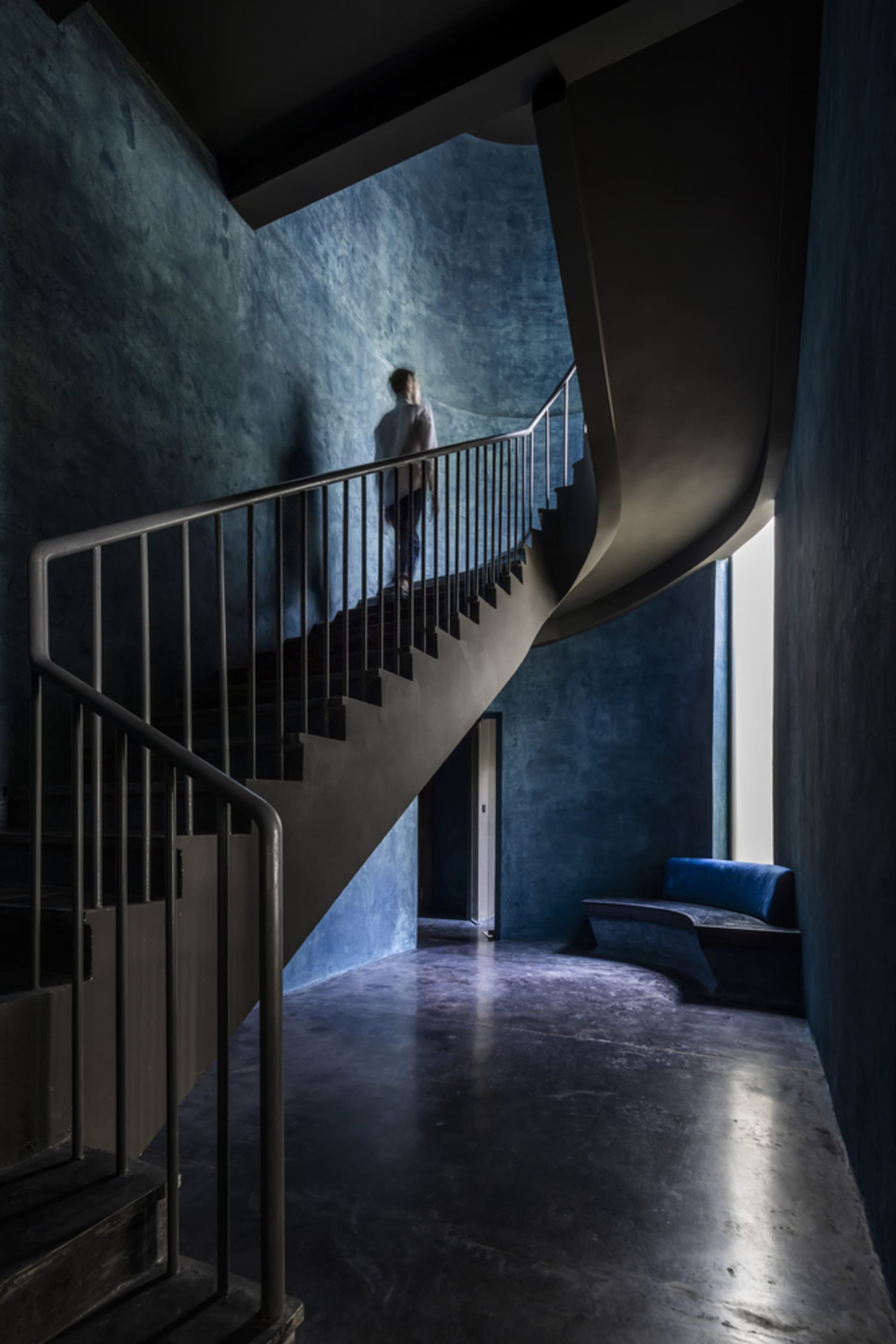 A modern, industrial-style staircase with concrete treads and metal railings, illuminated by natural light from a high window