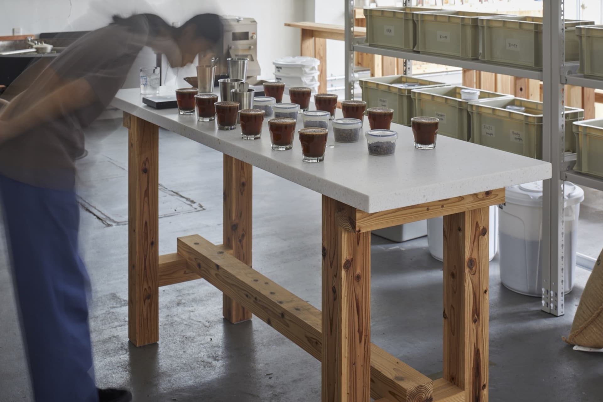 A spacious coffee tasting room featuring industrial design elements with a wood and concrete table and storage units.