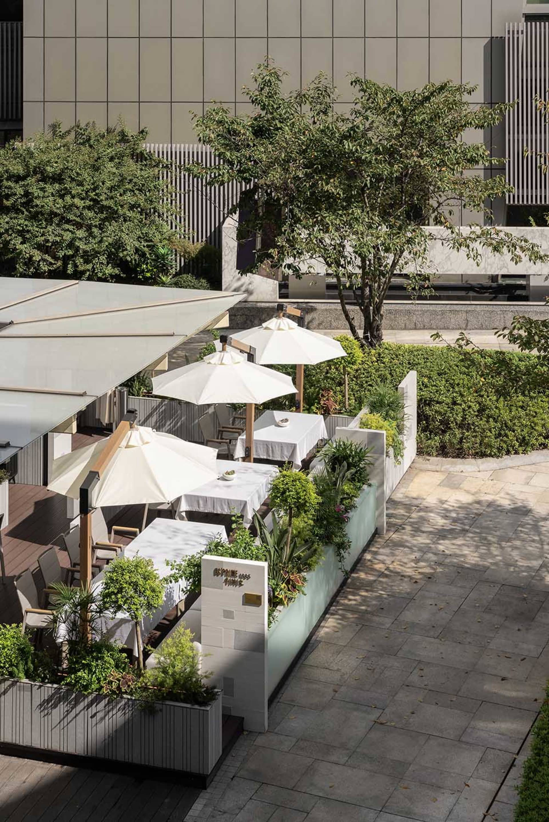 Outdoor seating area with white tables, umbrellas, and potted plants in a contemporary design setting.