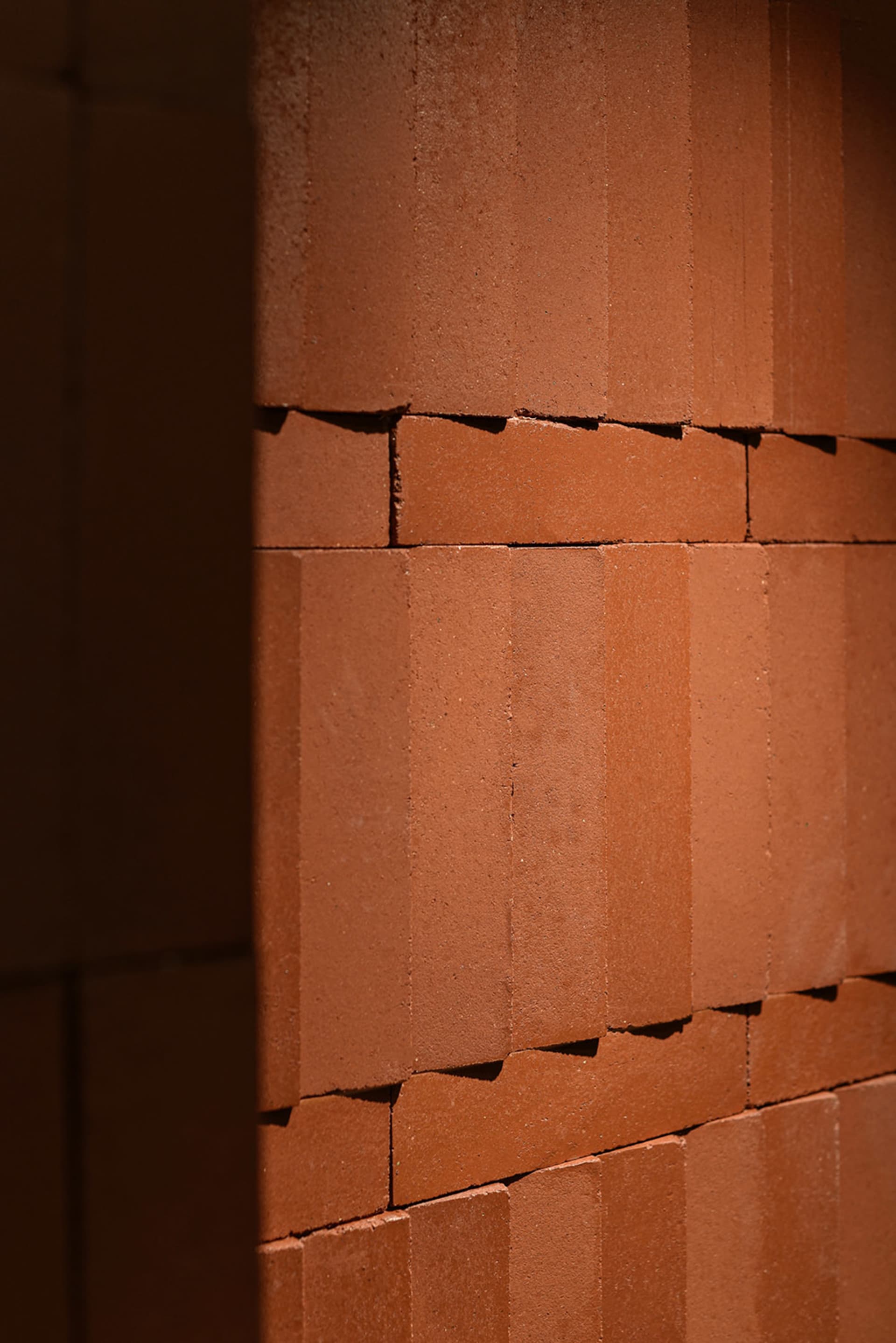 A textured brown brick wall with sunlight casting shadows on the surface.
