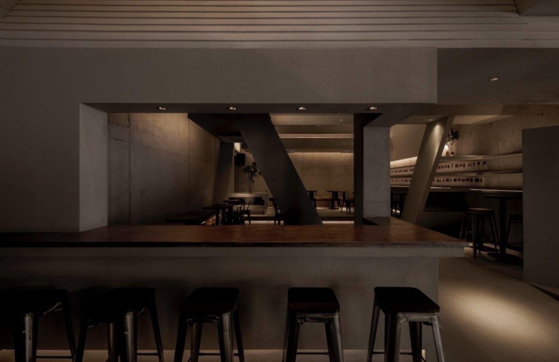 A minimalist industrial-style bar counter made of concrete, with stools in front of it and no customers.