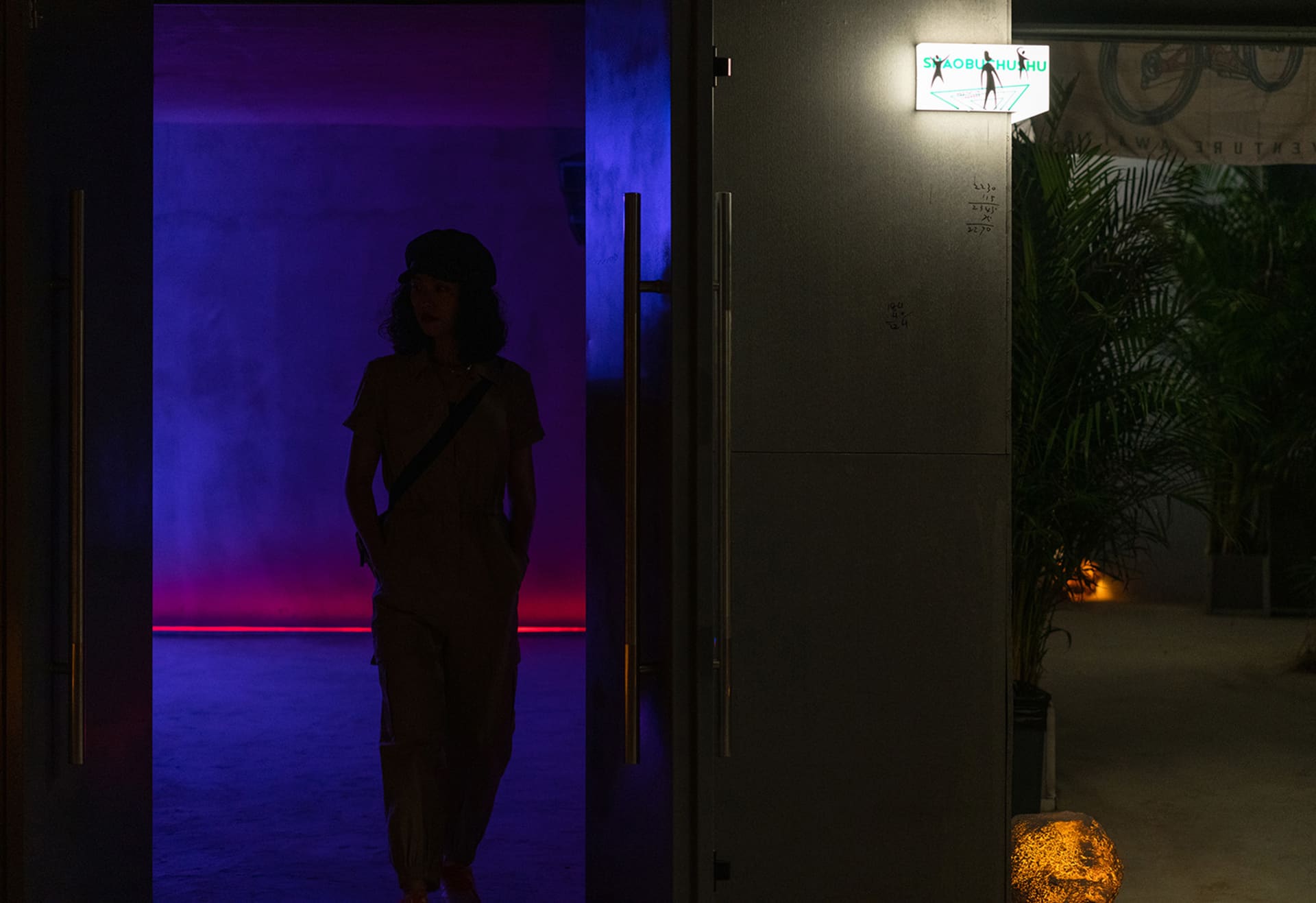 A silhouette of a person walking through an illuminated doorway in an urban setting.