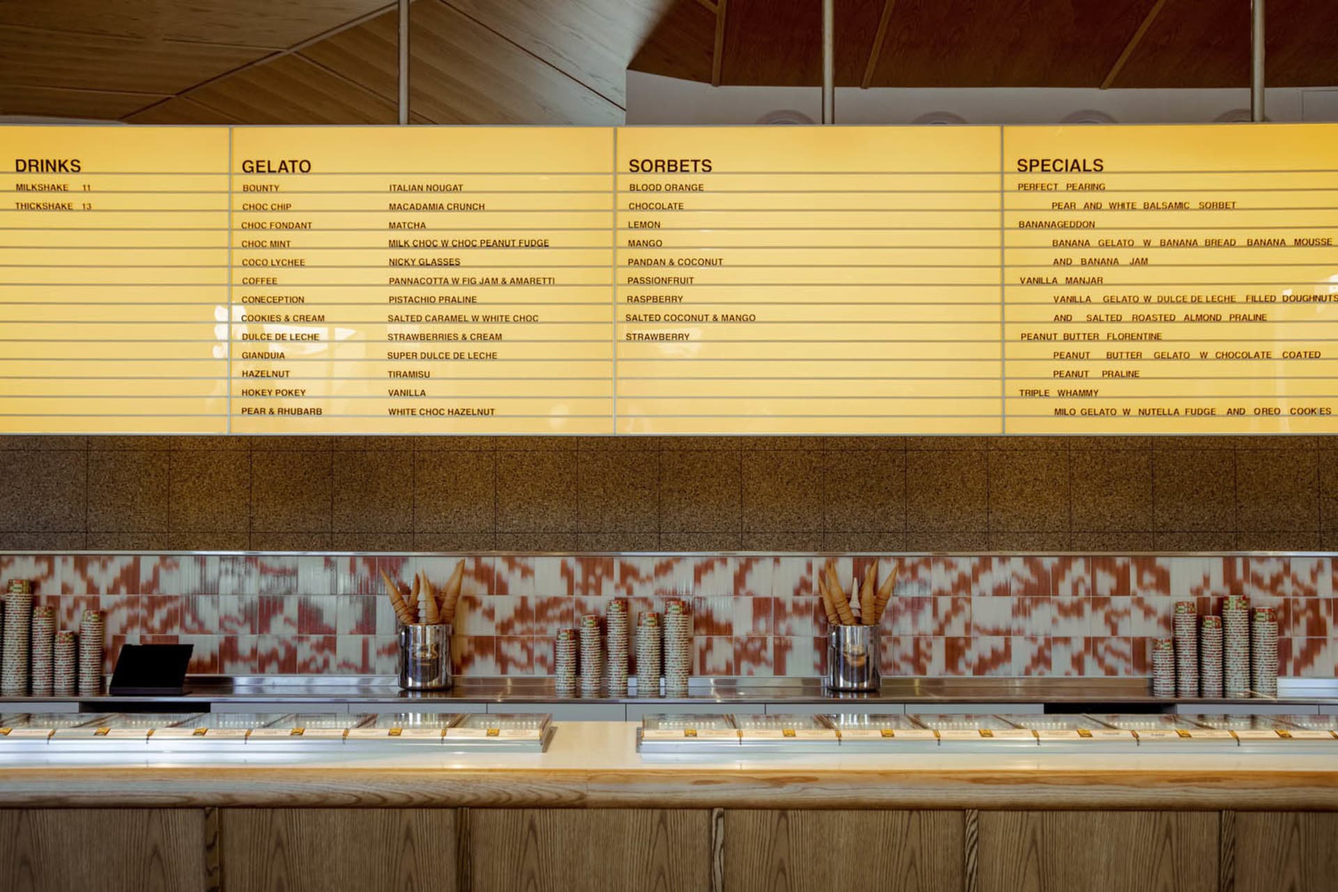 Gelato counter with tiled countertop displaying menu offerings.