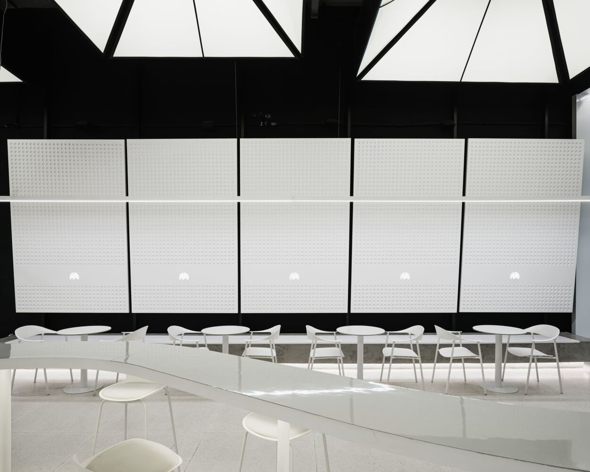A minimalist cafe interior with white tables and chairs, white beadboard walls, and a sleek white countertop.