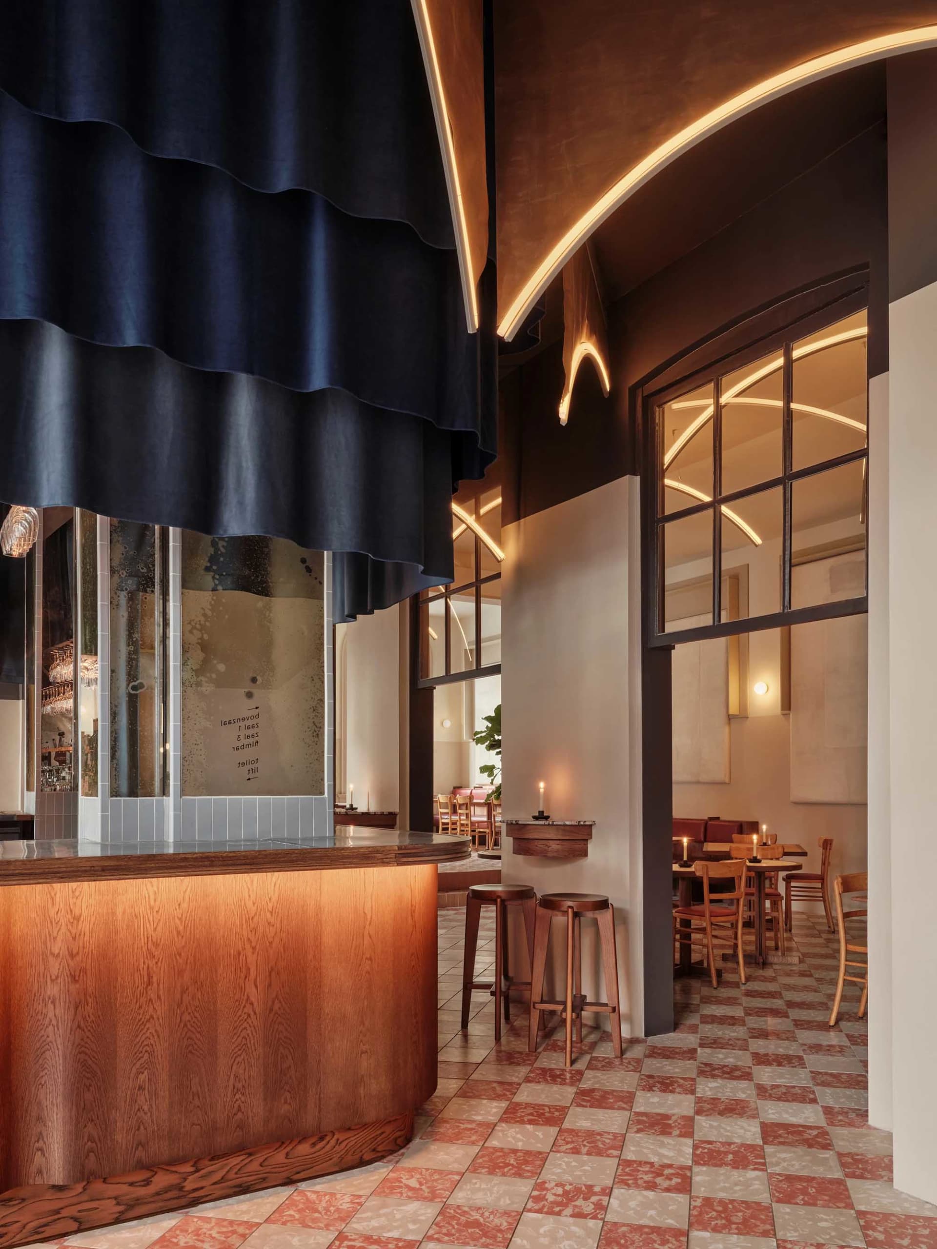 Interior of a modern restaurant with wooden bar counter, terrazzo flooring, and glass windows.