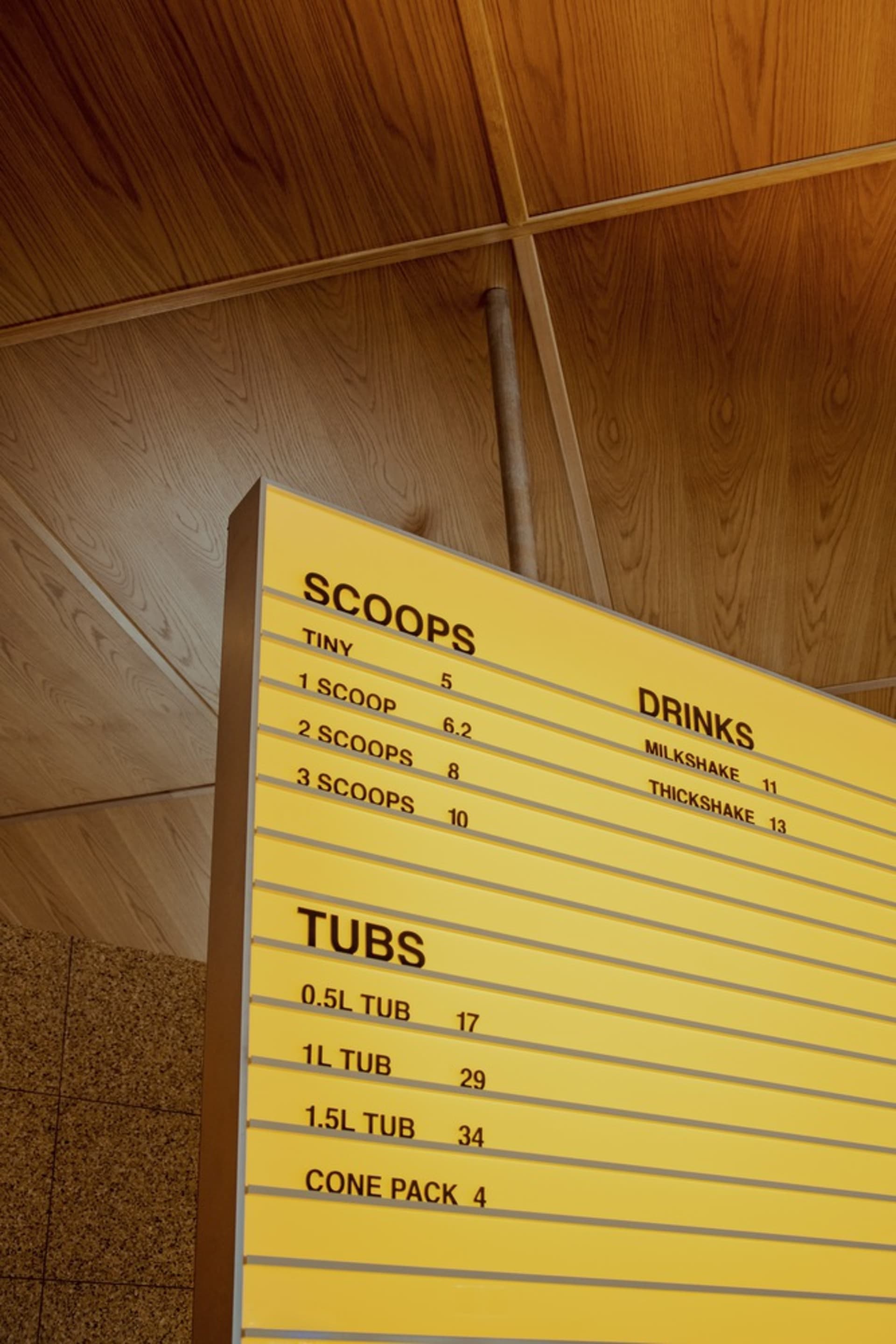Yellow cardboard menu board with scoops and drinks prices.