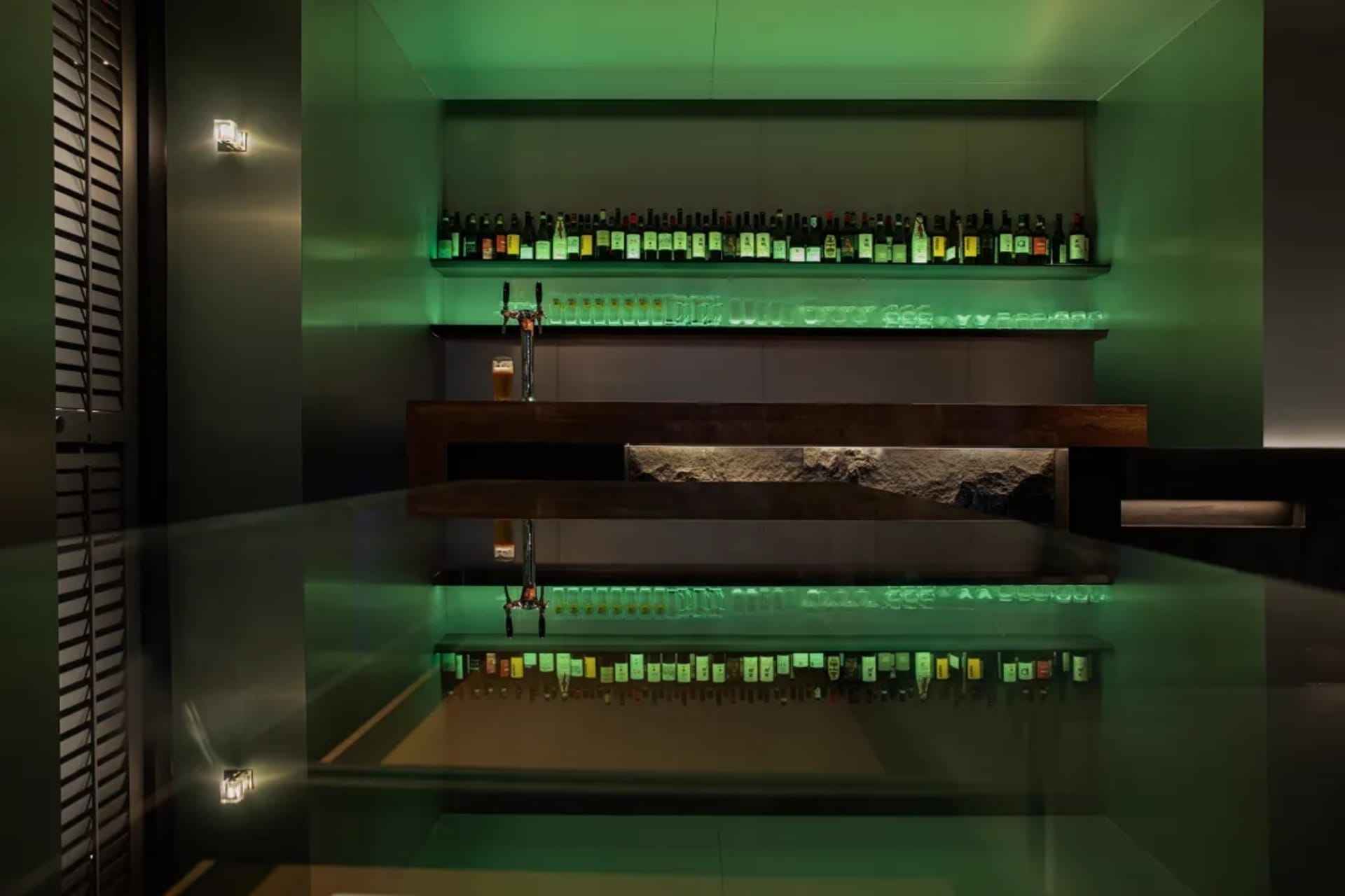 A modern bar interior featuring a steel and glass counter illuminated by green lighting.
