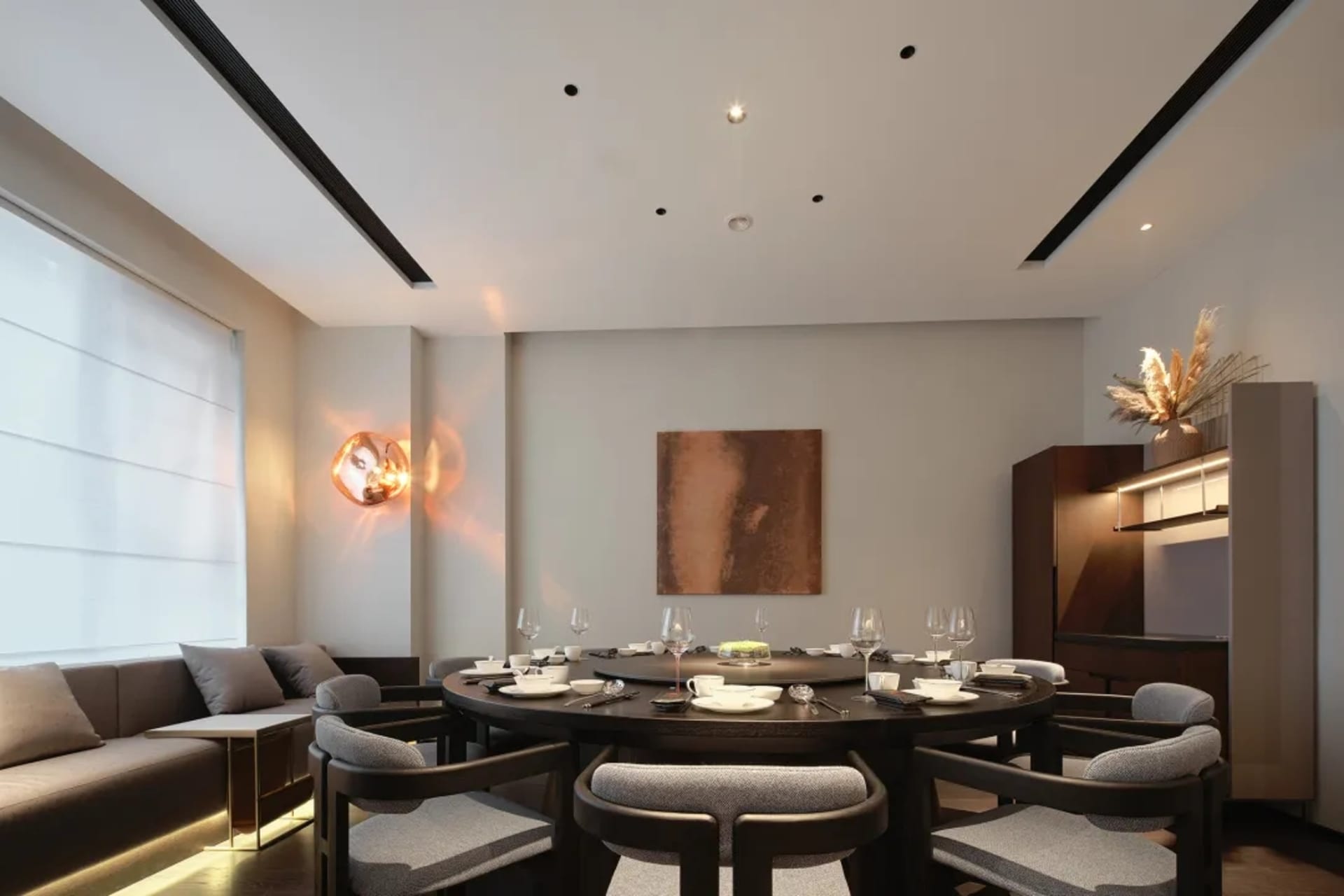 Modern residential dining room featuring a circular wooden table surrounded by upholstered chairs with cushions, a wall-mount