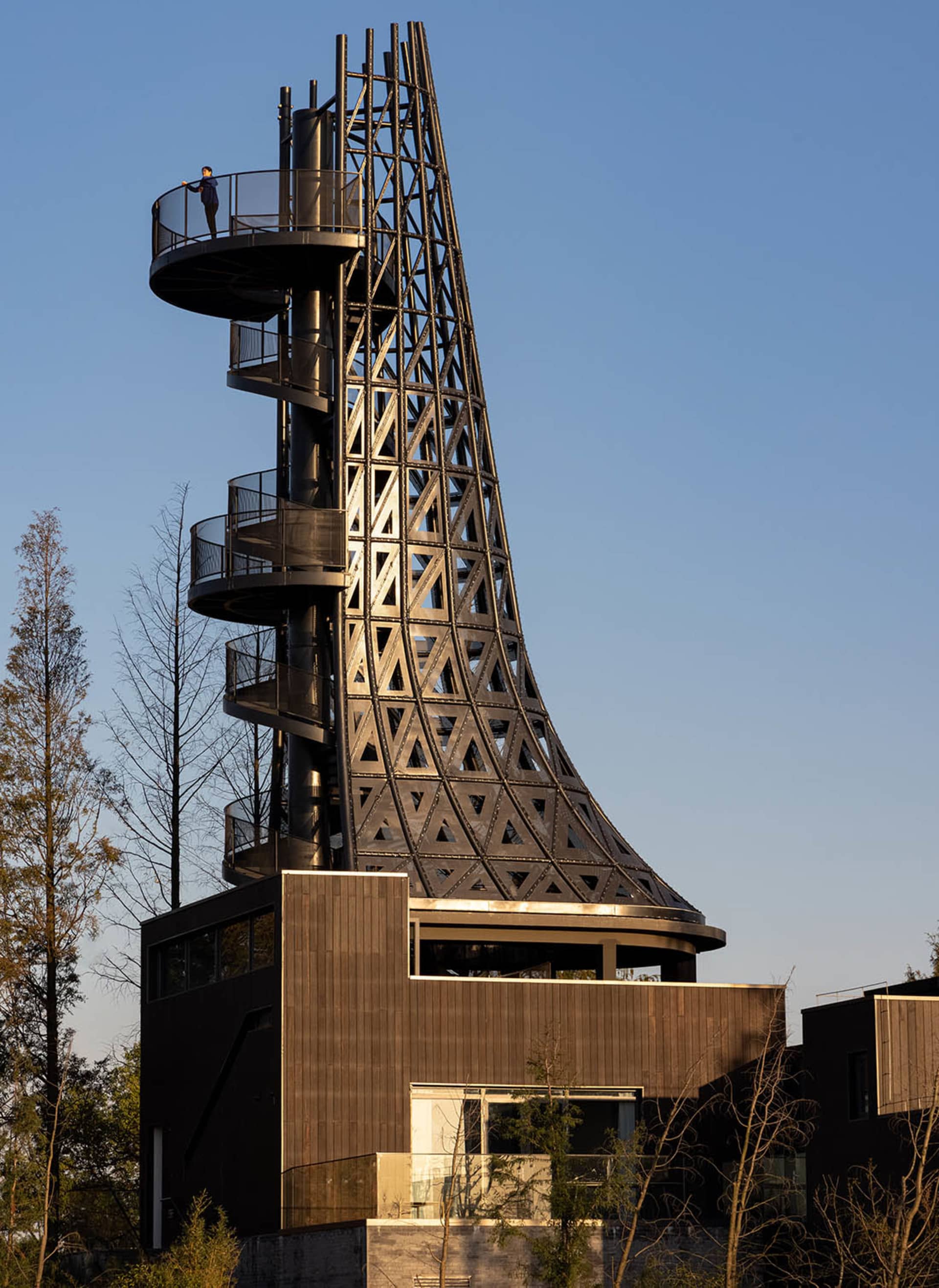 A modern metal observation tower with a spiral staircase and a person standing at the top.