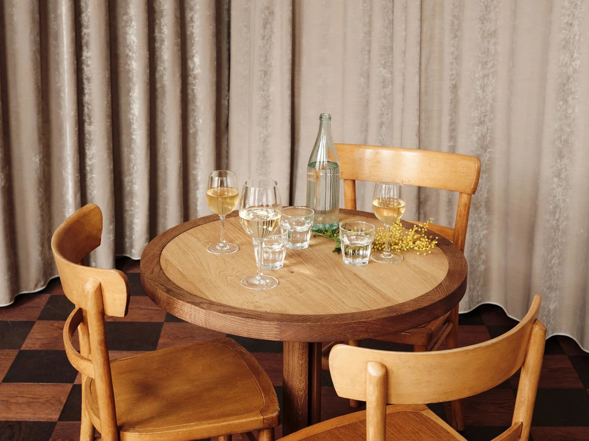 A modern restaurant setting featuring a wooden table with wine glasses and a water bottle.