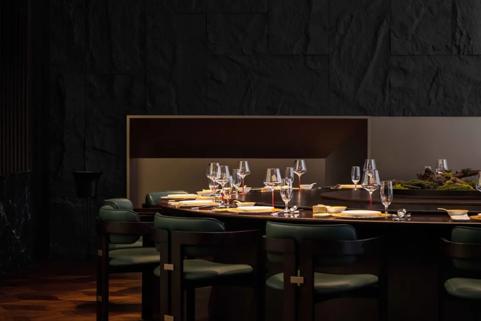 A modern restaurant interior featuring a circular dining table with black marble material and green chairs.