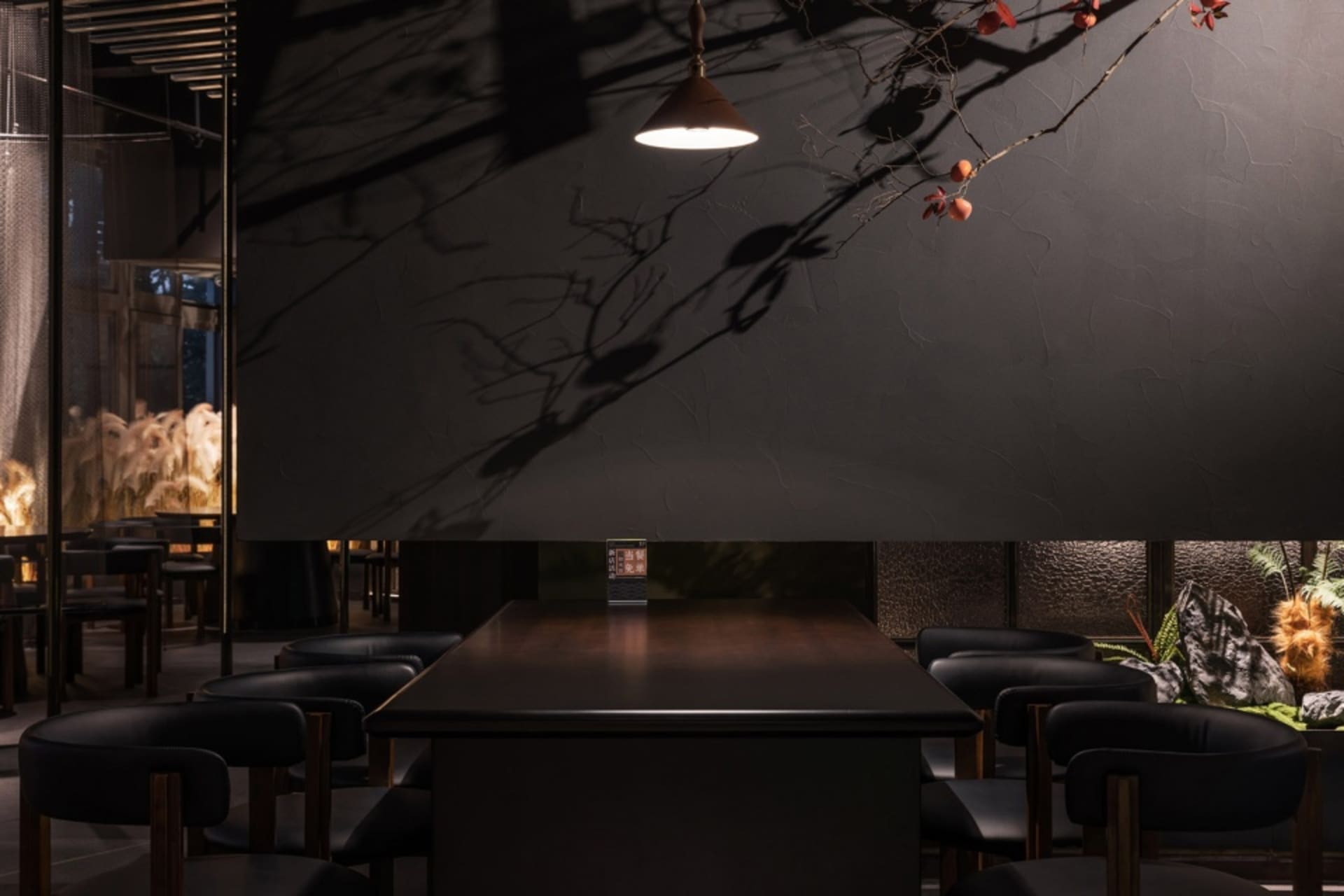 A modern restaurant interior with black walls, dark wood furniture, and a black stone counter, featuring a patterned glass pa
