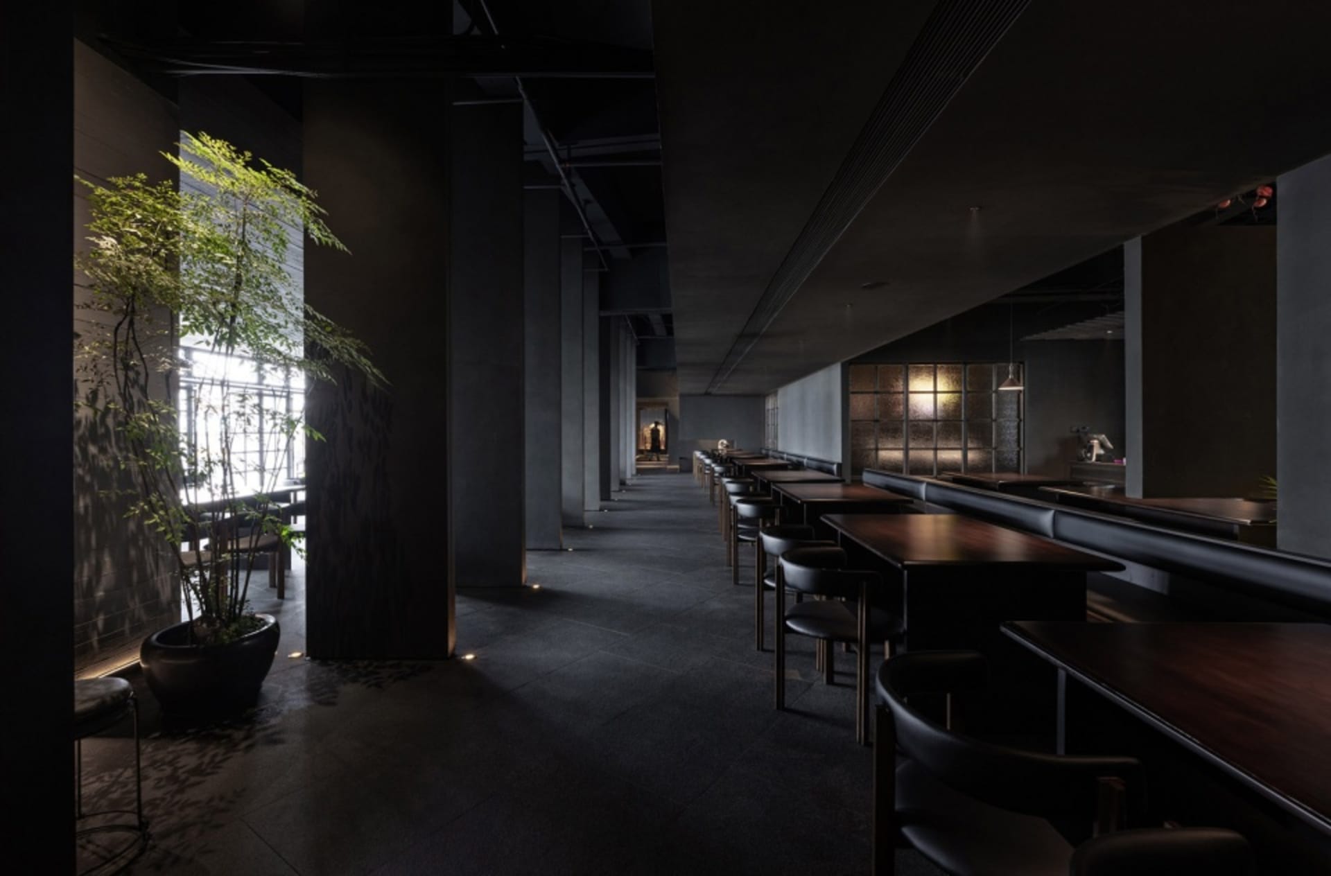 Modern restaurant interior with concrete walls, glass panels, and metal furniture.