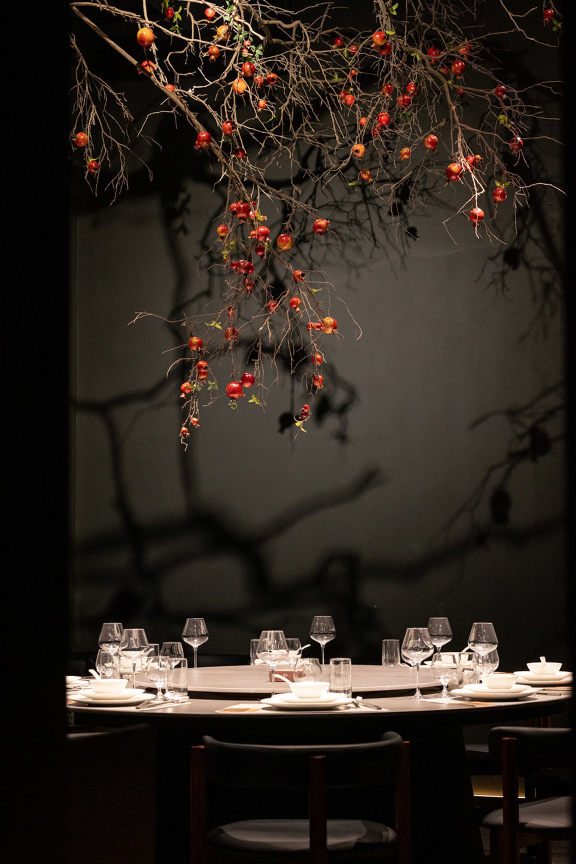 A modern restaurant setting with glass branches adorned with red pomegranates.